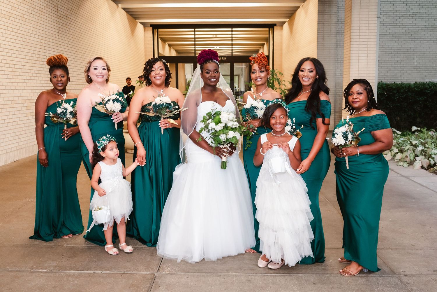 Wedding party poses in coordinating emerald green dresses with flower girls in white.