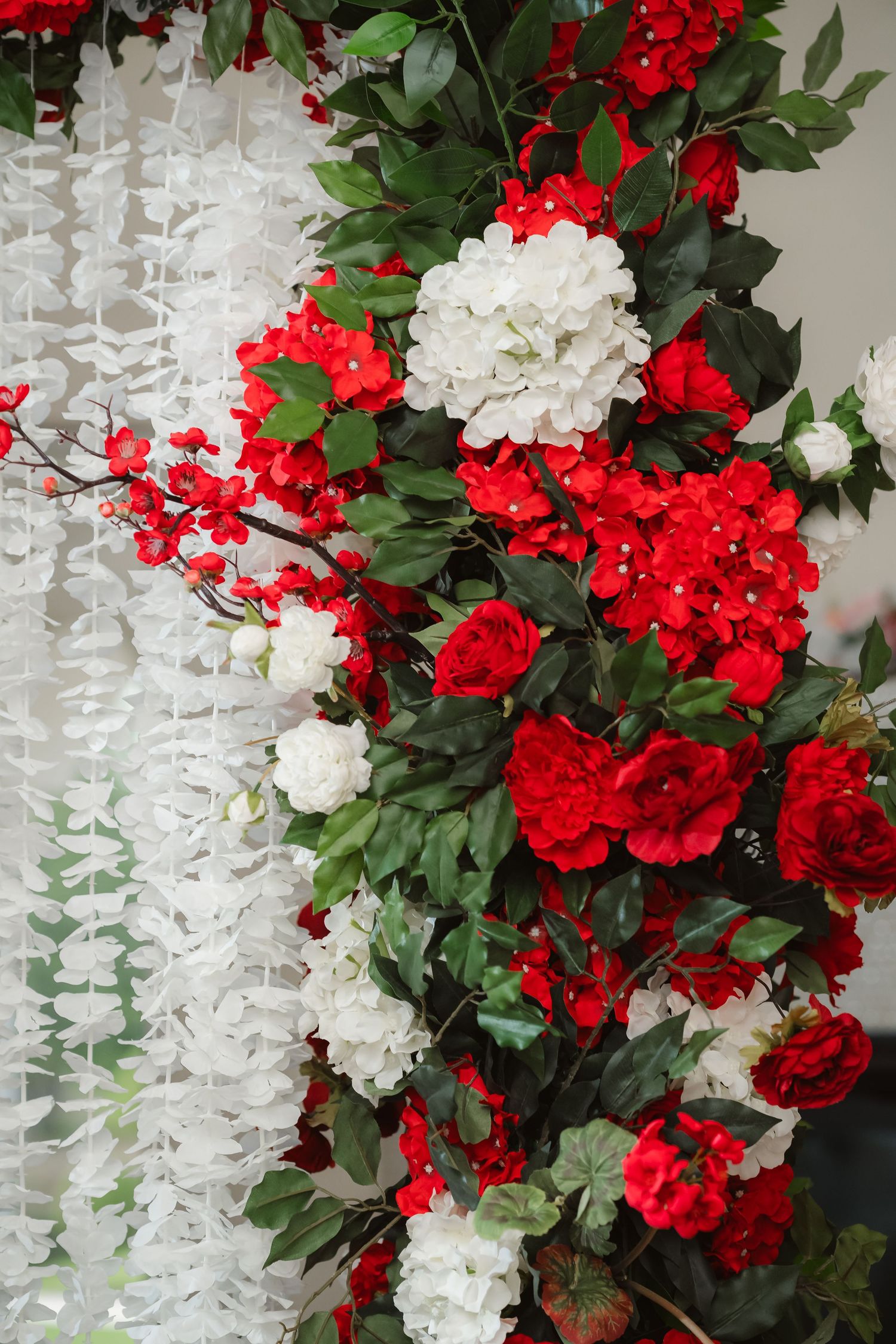 Beautiful red and white floral wedding decorations with cascading flowers and greenery against a white backdrop.