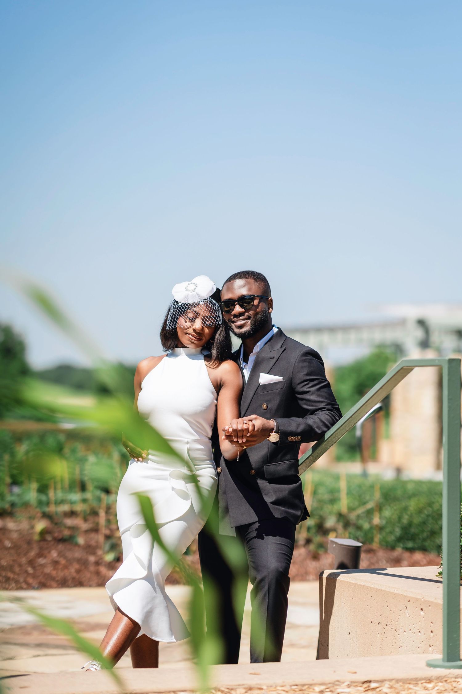 A couple in formal attire poses together on outdoor steps, with the bride wearing a white dress and groom in dark suit.