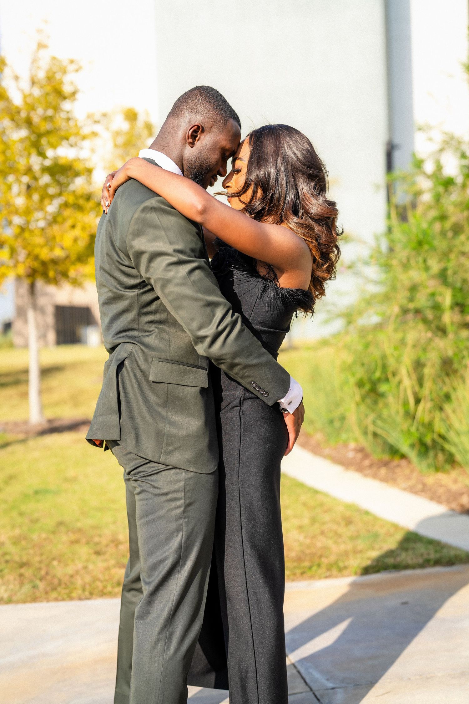 A couple embraces joyfully outdoors after a proposal with fall foliage in the background.