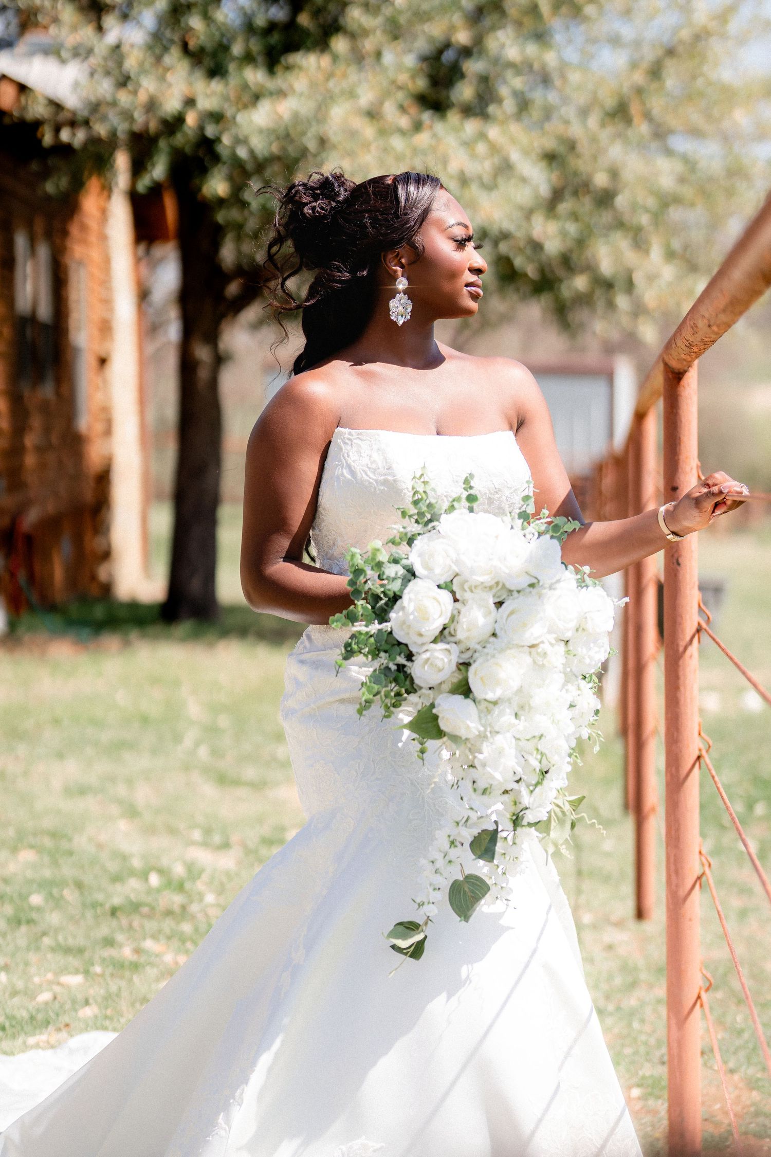 Elegant white wedding dress with flowing train and white floral bouquet captured in outdoor bridal portraits.