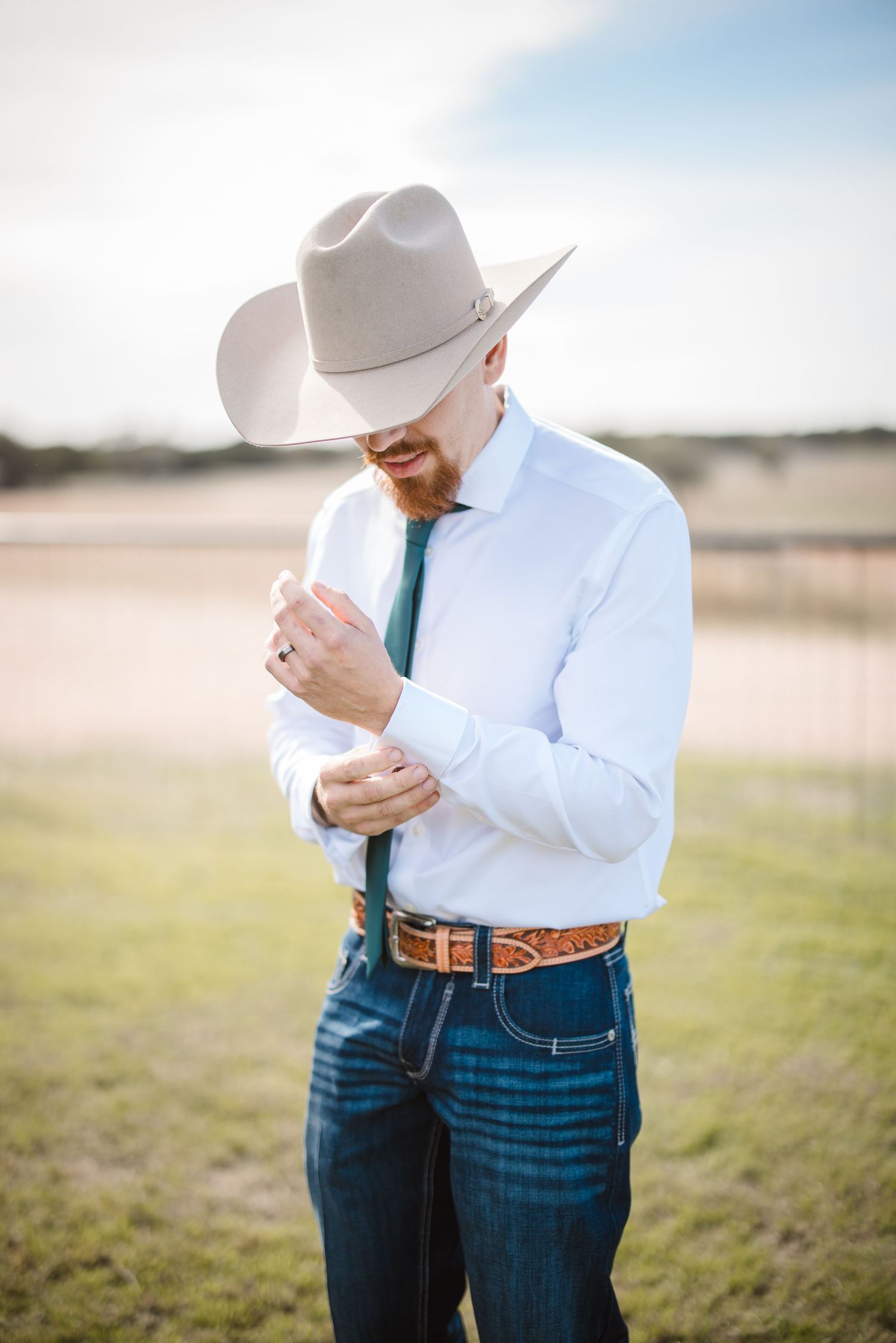 Person in white western shirt and cowboy hat with jeans showing emotional reaction outdoors.