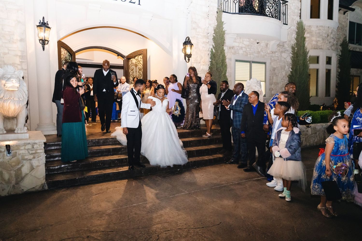 Wedding guests gather outside stone venue at dusk with lanterns illuminating the entrance.