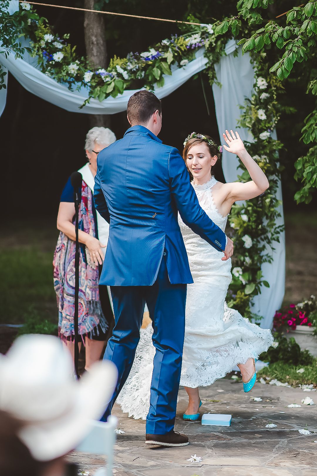 A couple shares their first dance under a white draped ceremony arch decorated with greenery.