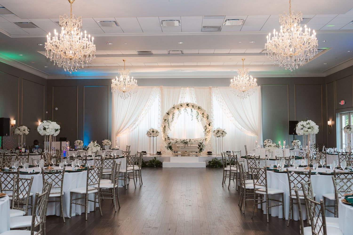 Elegant wedding reception ballroom with crystal chandeliers, white draping, and silver chiavari chairs.