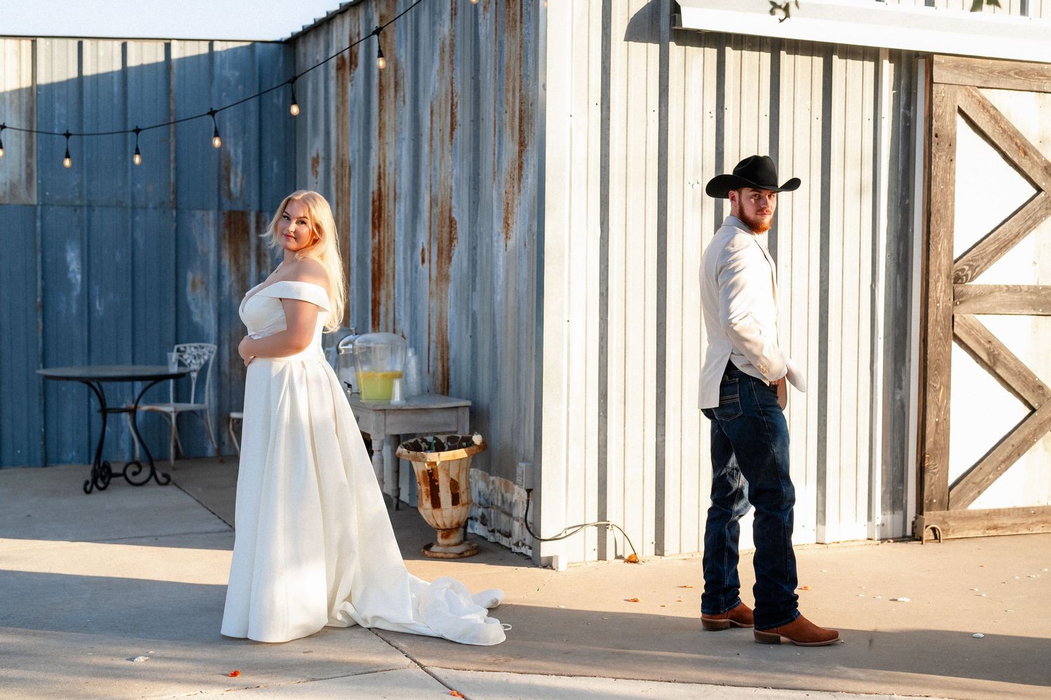 A couple in wedding attire stand apart against a rustic barn wall during a first look moment.