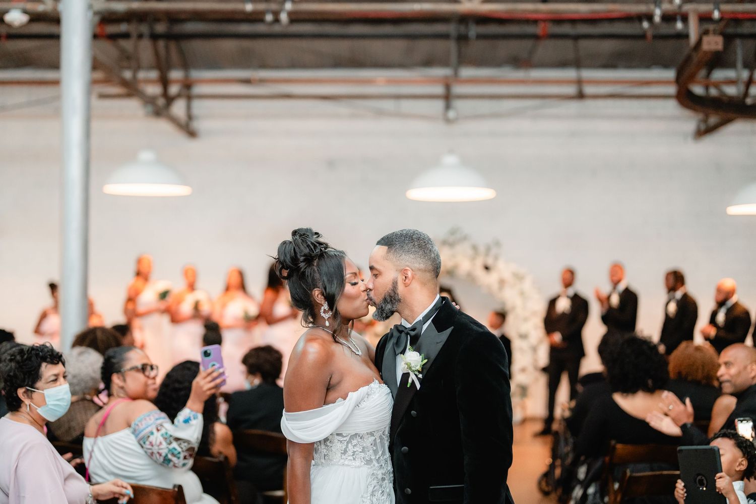 Wedding reception celebration with guests dancing under industrial pendant lighting.