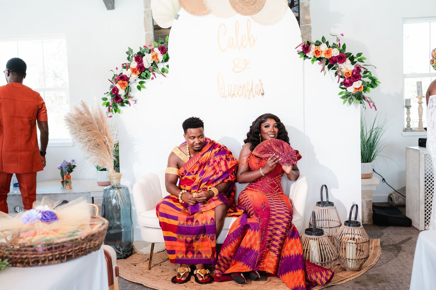 Colorful celebration gathering with people seated in a bright white room with floral decorations.
