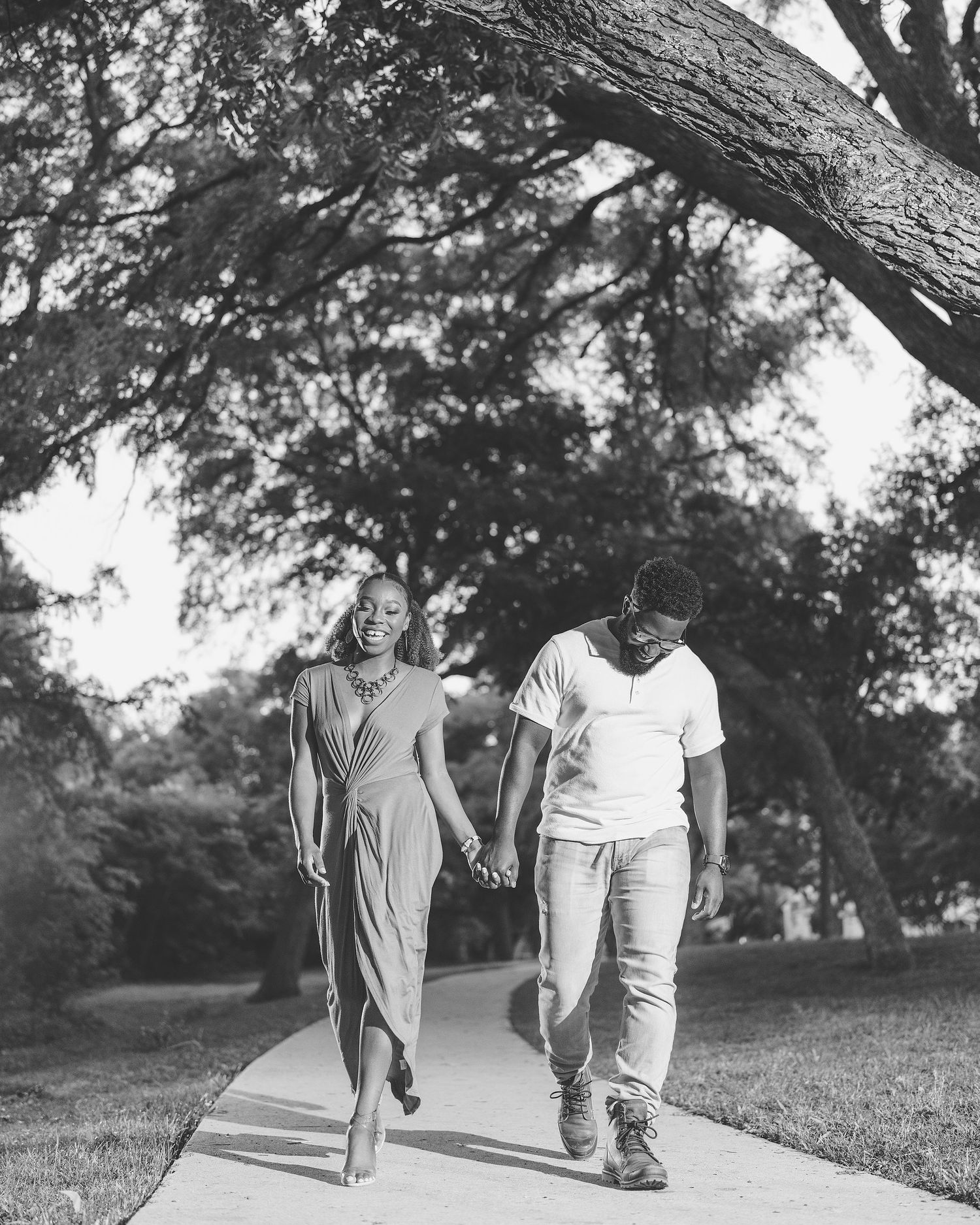 A couple walks together on a park path in black and white photography.