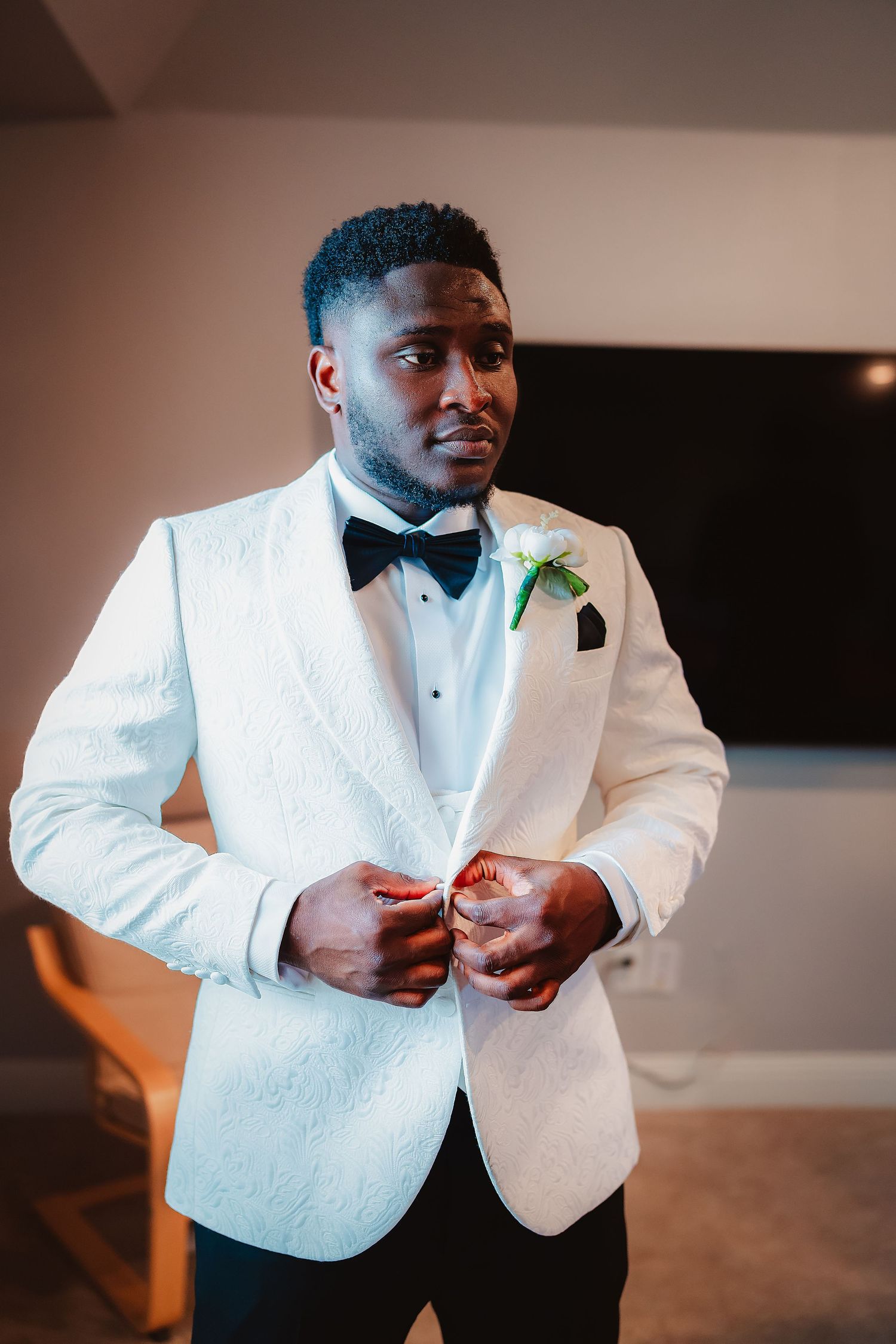 Groom adjusts his white tuxedo jacket and bow tie while getting ready for the wedding ceremony.