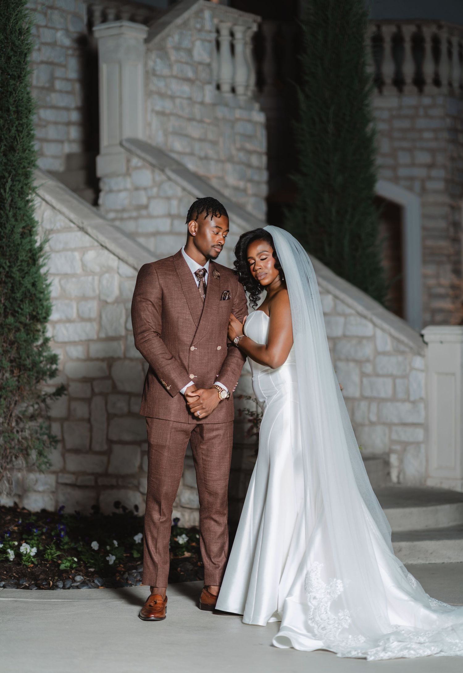 Romantic wedding portraits against stone wall backdrop with groom in brown suit.