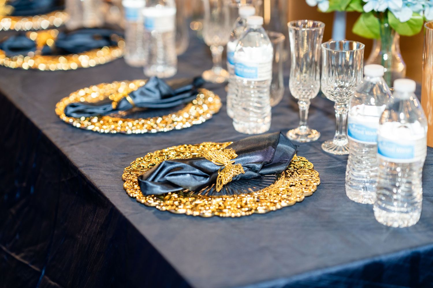 Navy blue table settings with gold charger plates and water bottles arranged for an elegant dining experience.