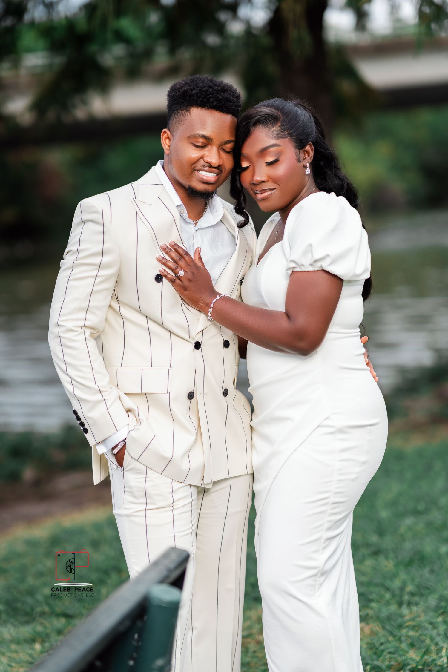 A couple in matching white outfits embrace outdoors during a romantic photoshoot by a lake.