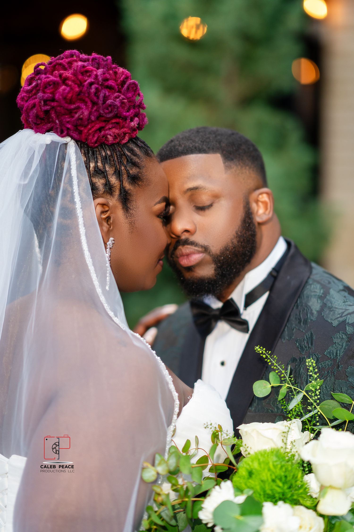 A romantic wedding couple shares an intimate moment outdoors with white and burgundy floral decorations.