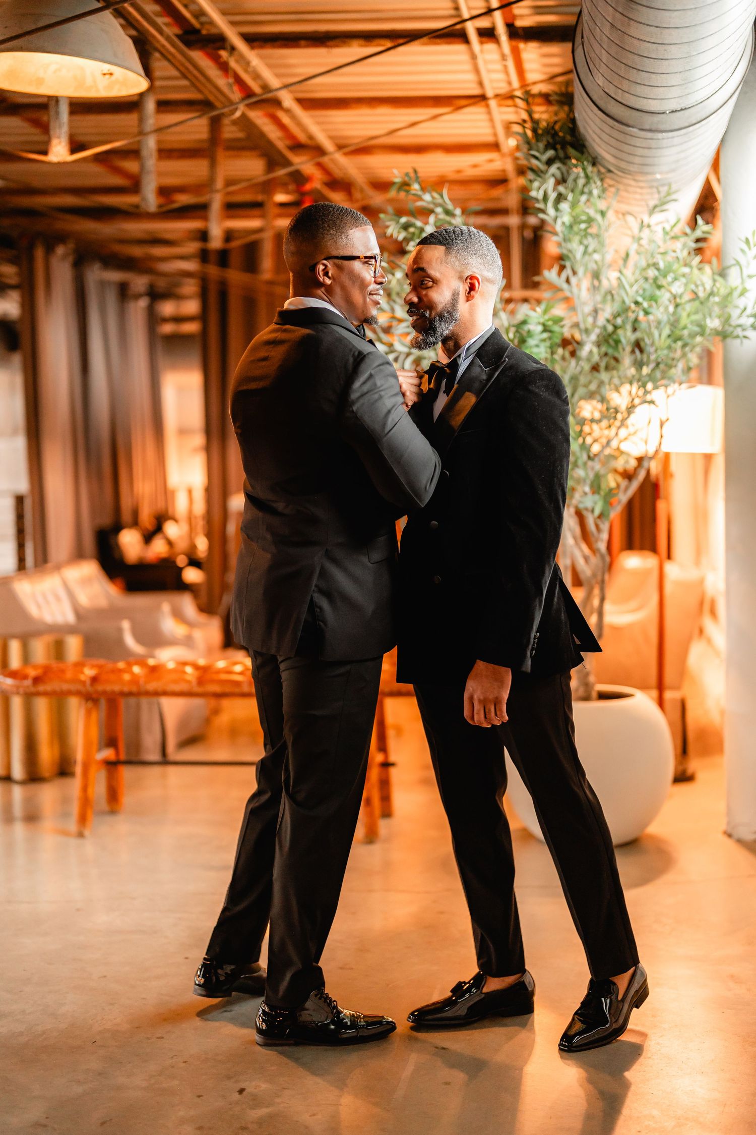 Wedding party members in formal attire interact playfully in rustic venue.