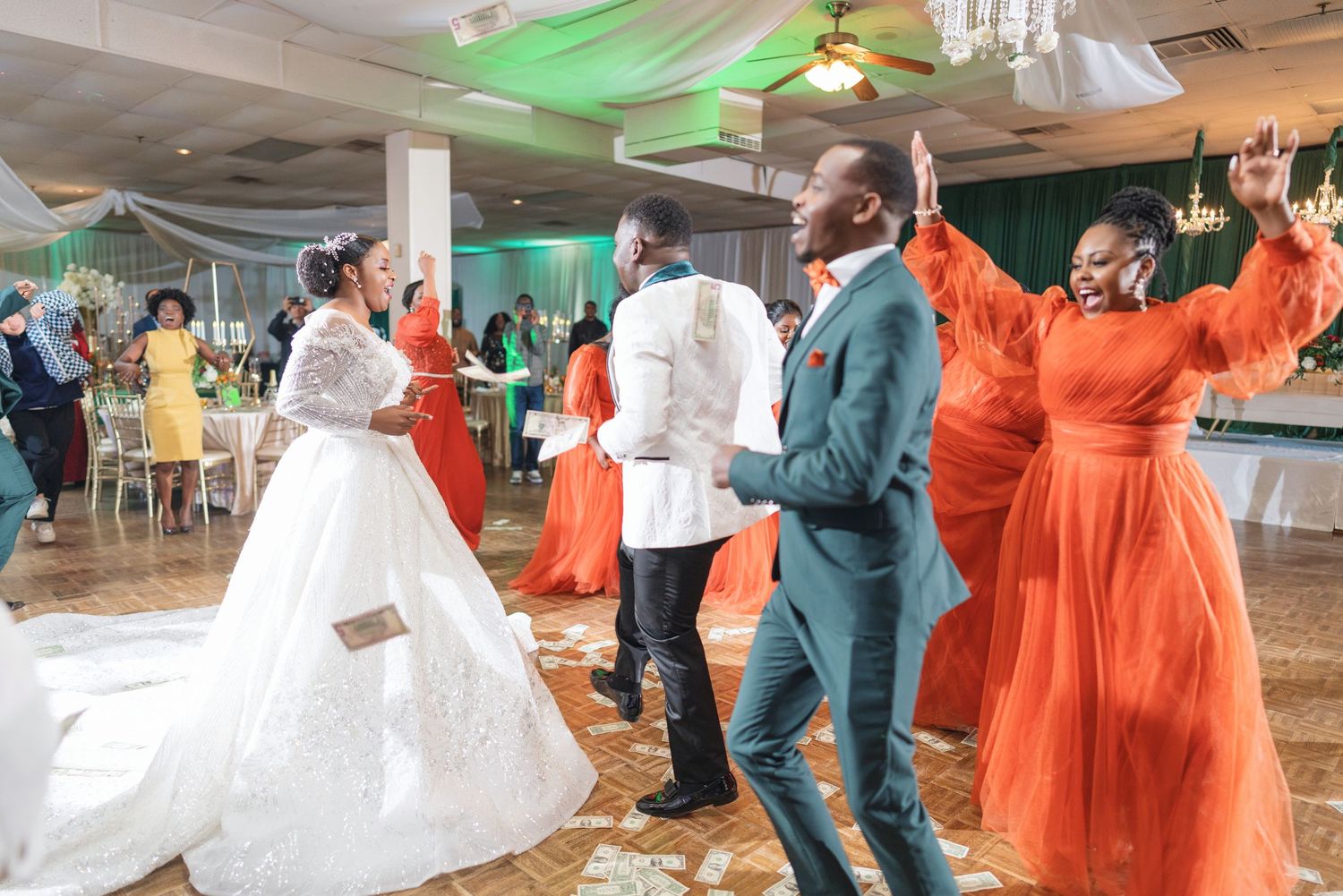 Wedding reception dance floor with guests in orange and white attire celebrating.