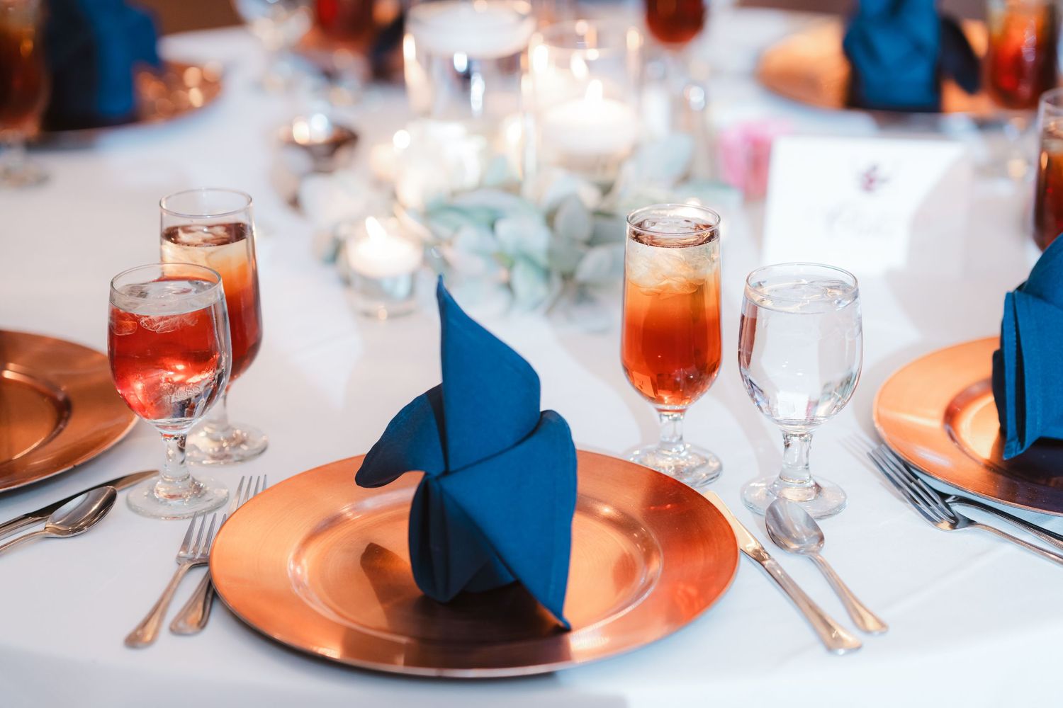 Wedding reception table settings with coral charger plates, glassware and navy blue accents.