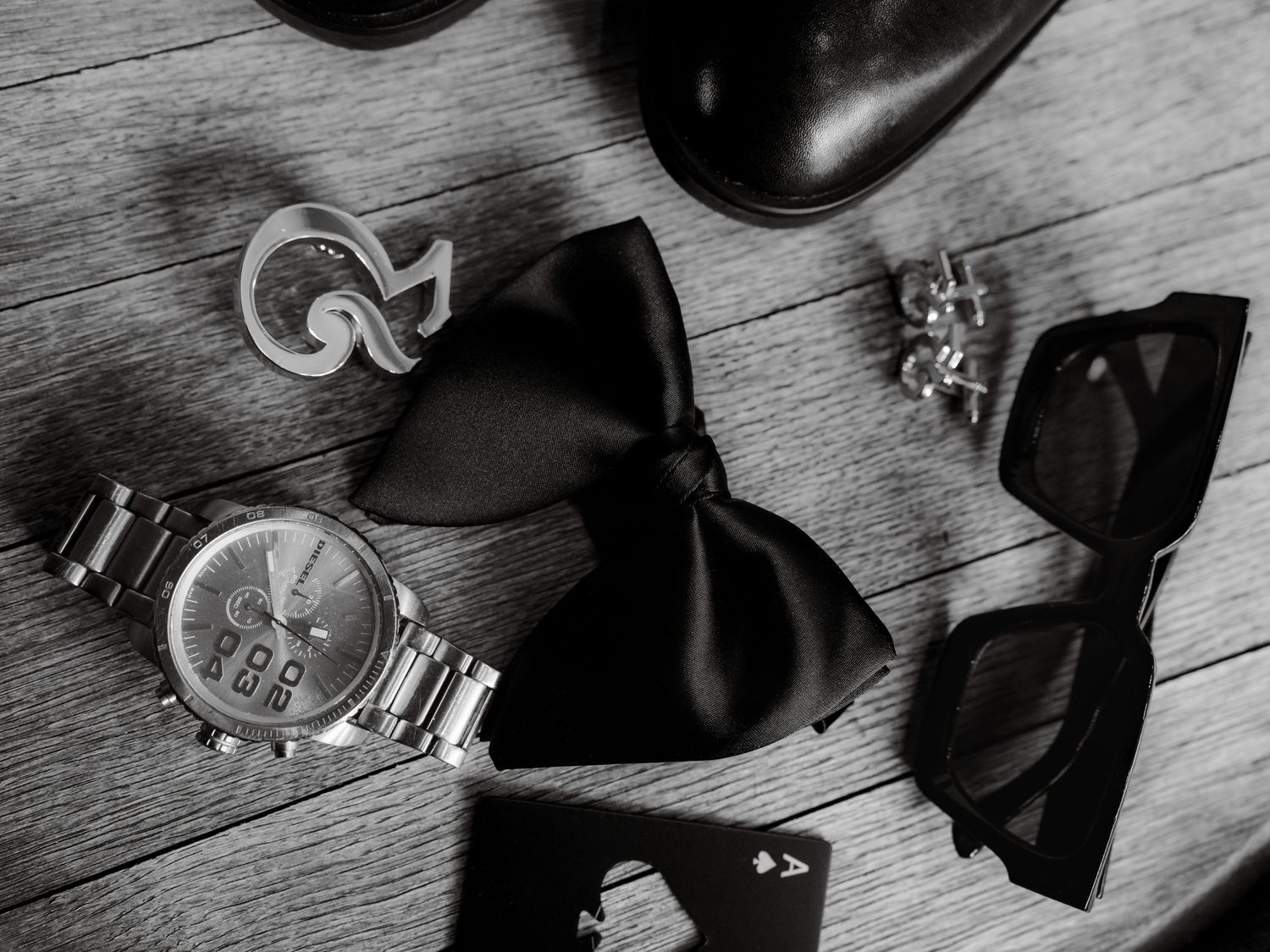 Black and white detail shot of formal shoes and accessories on wooden floor.