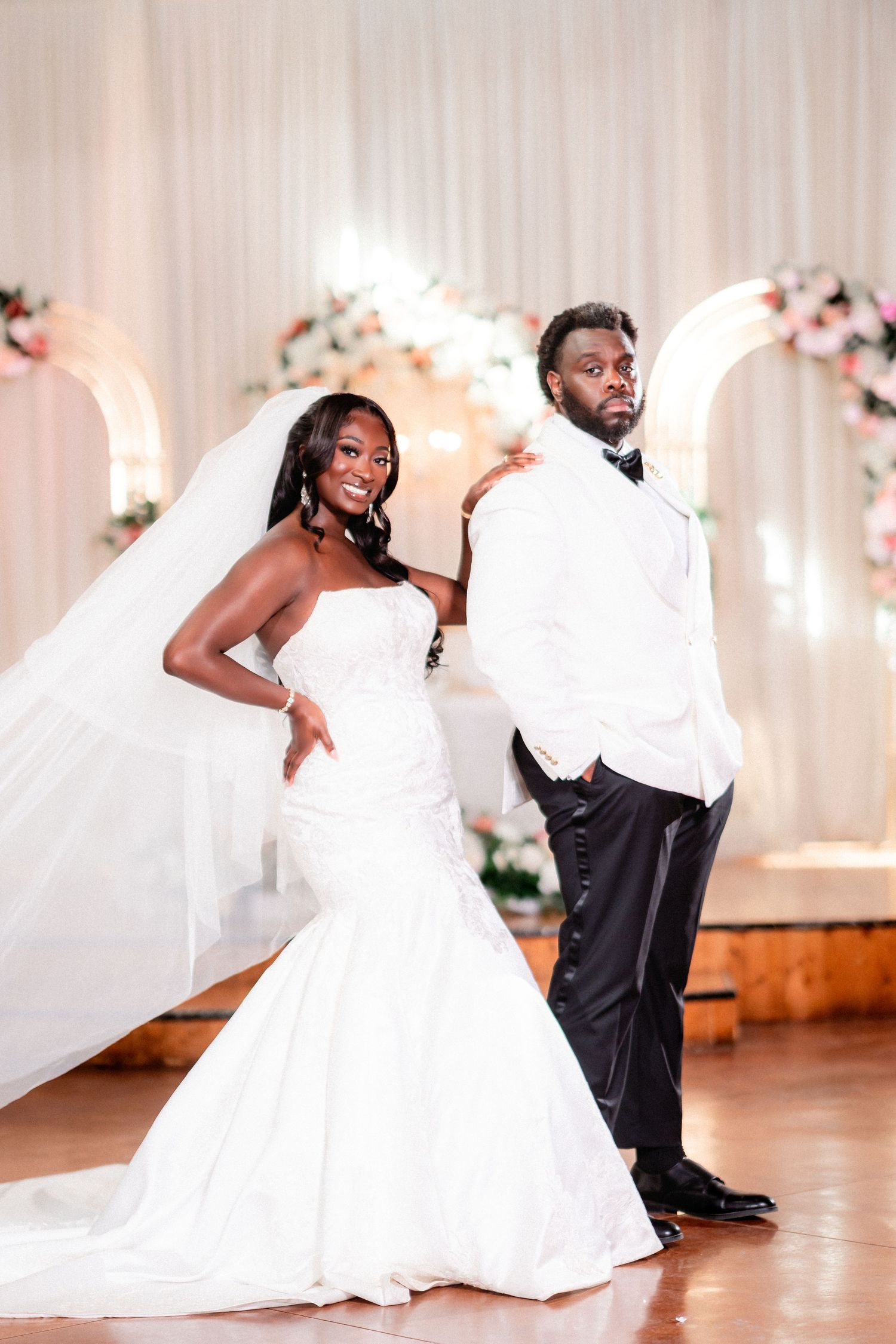 A couple strikes a stylish pose under floral arches at their wedding reception.