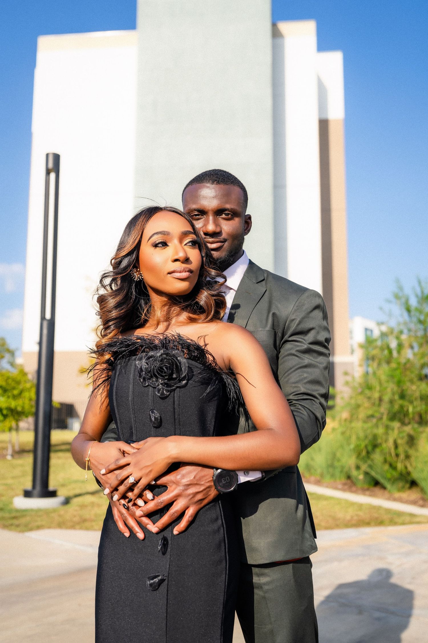 A couple embraces during their engagement photos against white pillars on a sunny day.