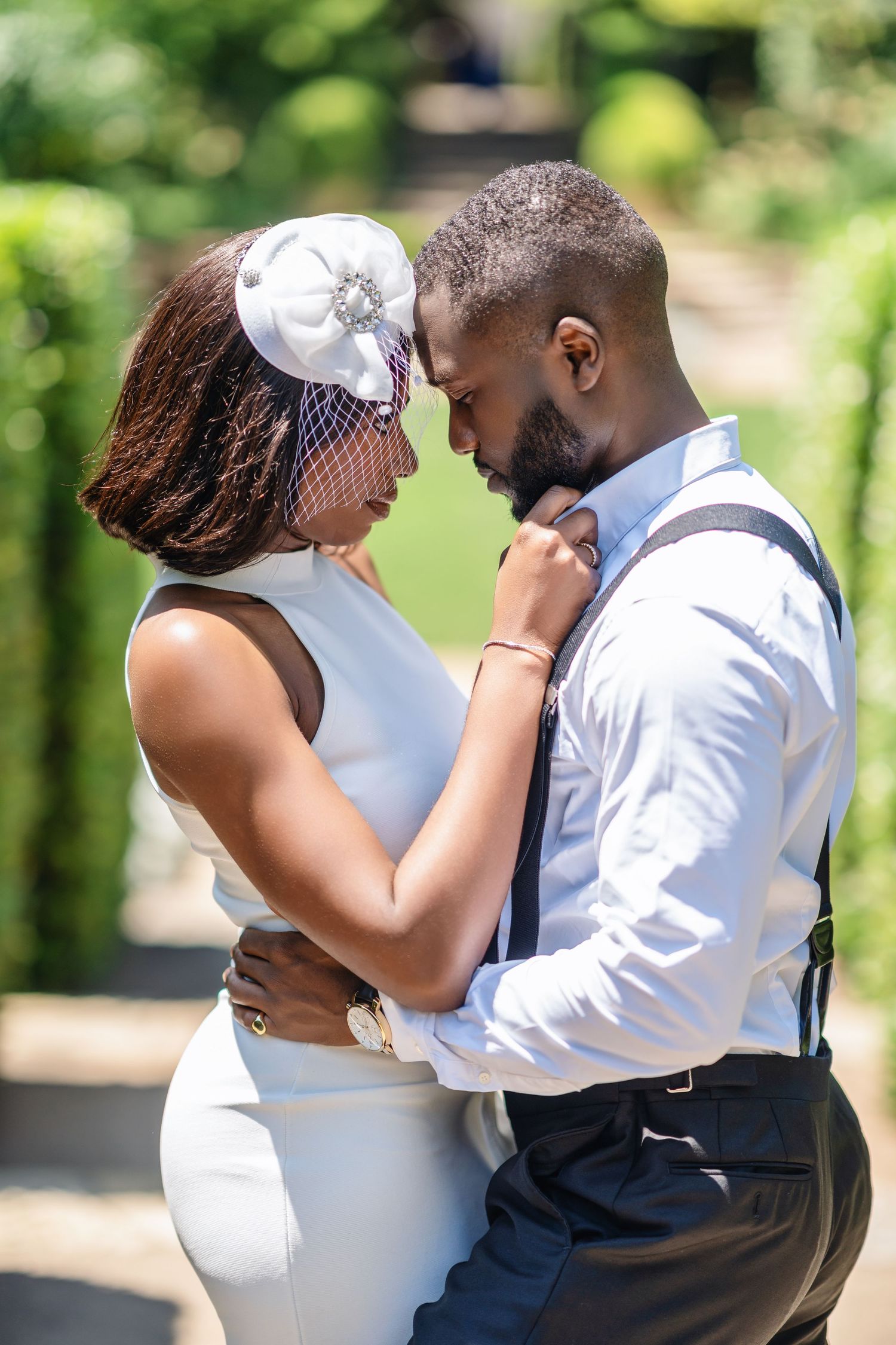 A couple embraces in an intimate moment surrounded by lush green foliage.