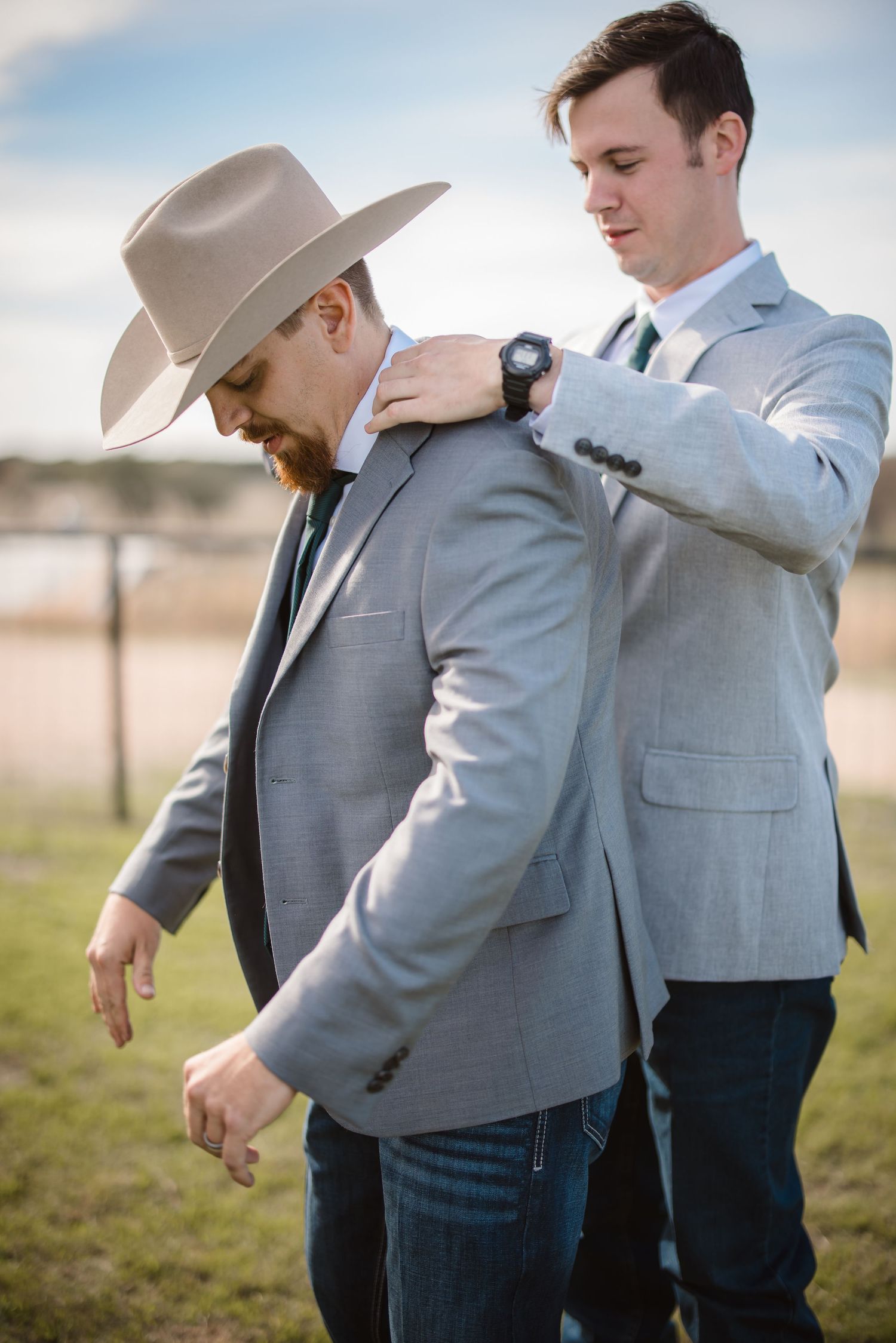 Men in gray suits and western wear showing off dance moves in an outdoor setting.