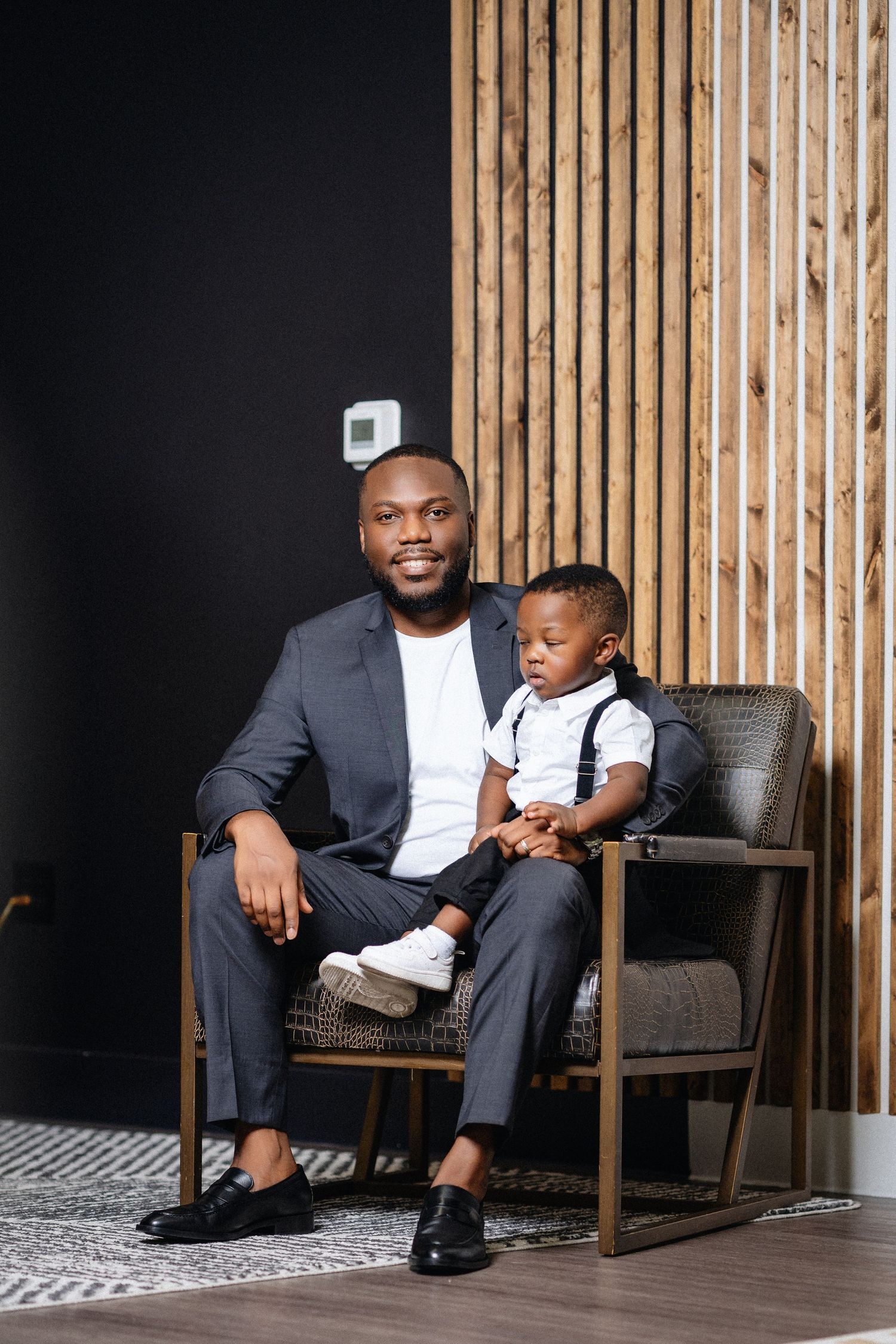 A series of four photos showing a father and child sitting together in a modern chair against a wooden slat wall.