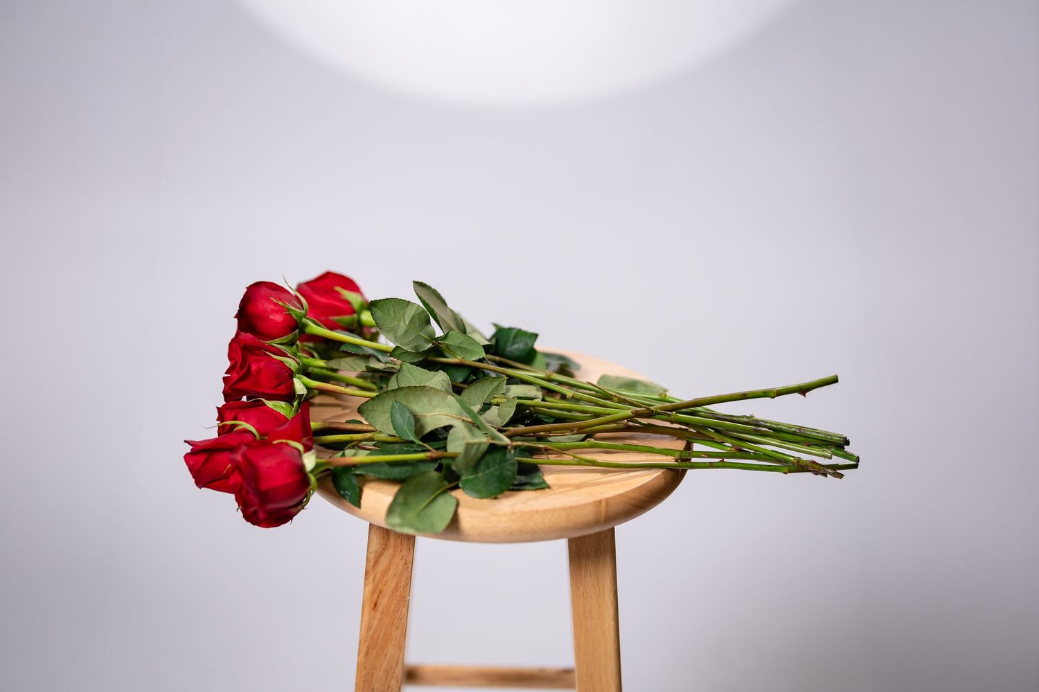 A bouquet of fresh red roses lying on a wooden stool against a gray background.
