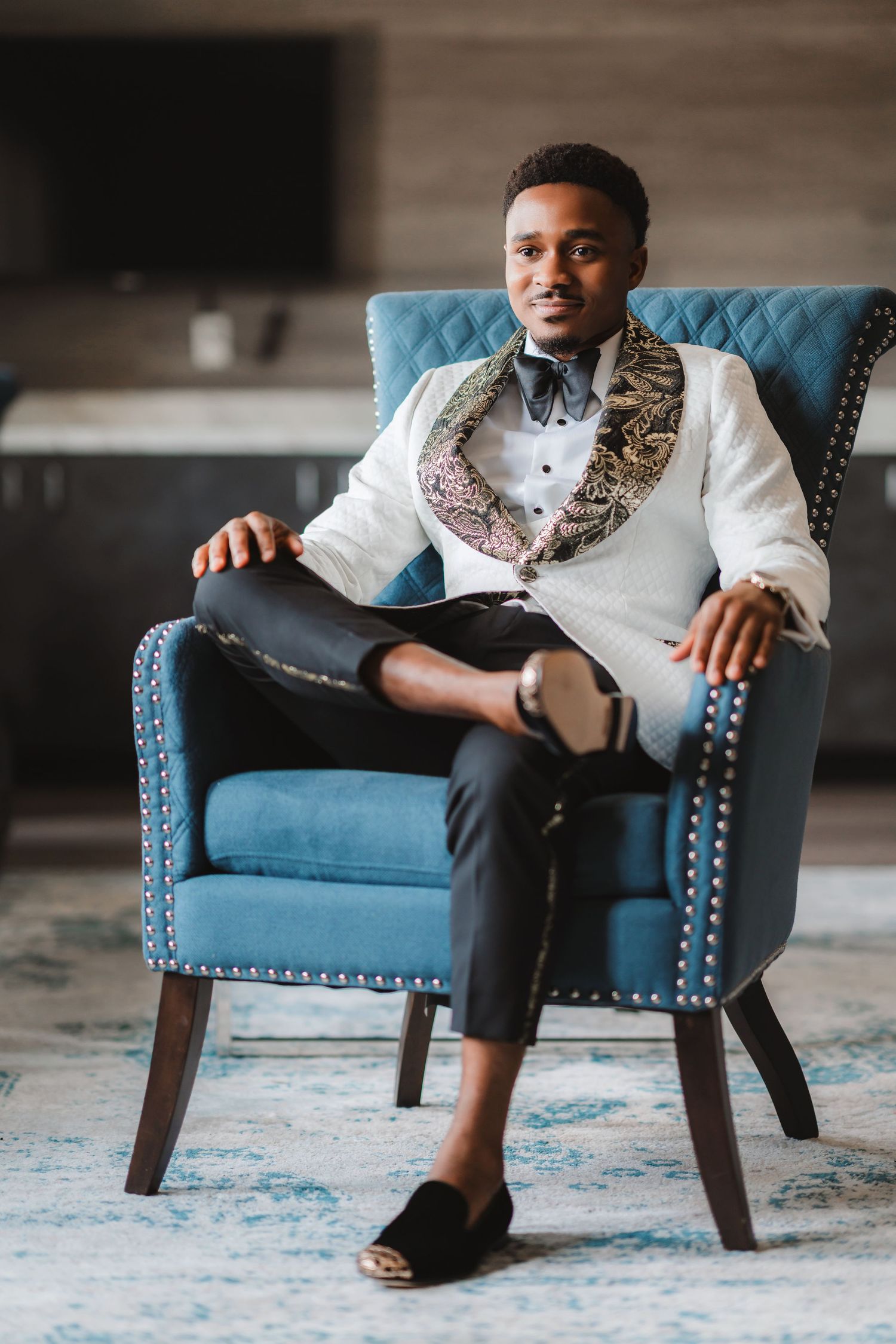 A person sits in a blue upholstered armchair wearing a white dress shirt and dark pants.