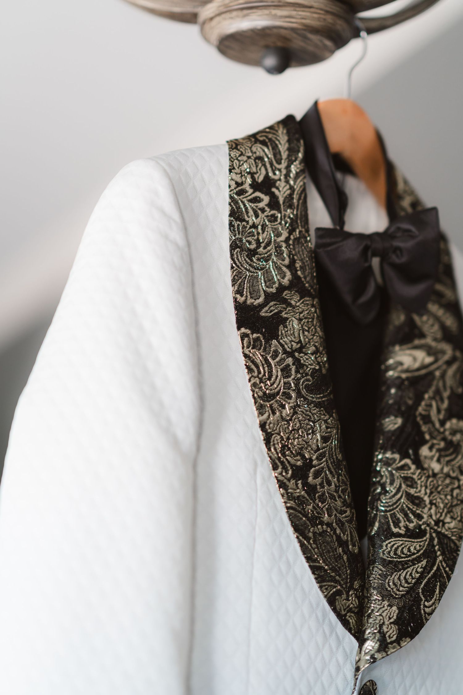 Detail shot of white textured jacket with black and gold floral pattern lapel.