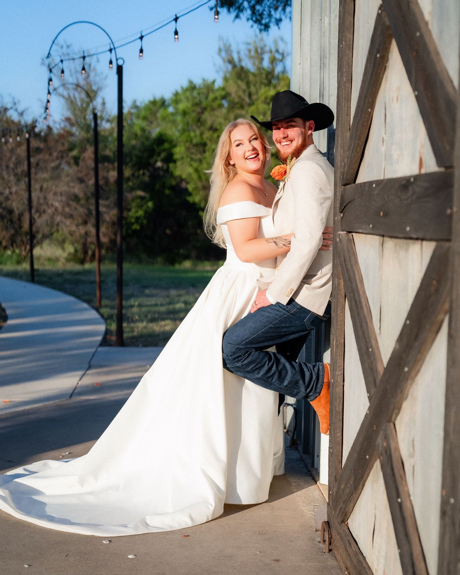 Wedding couple poses against a rustic barn wall with string lights in the background.