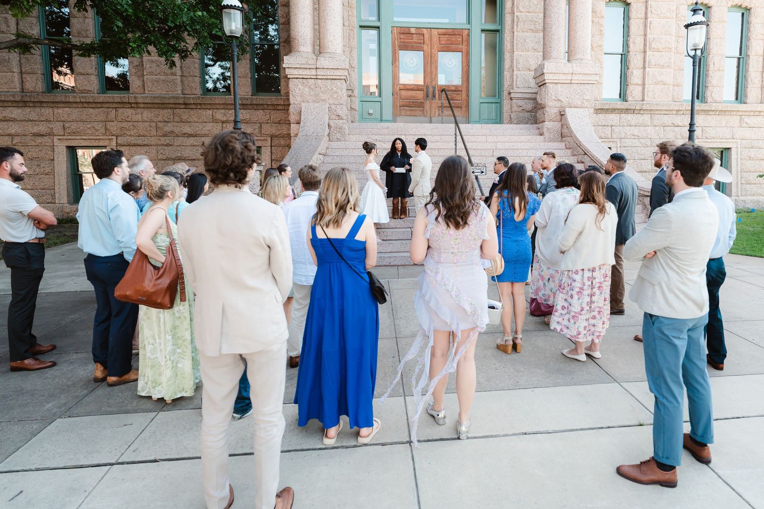 Wedding guests gather outside a building for a ceremony.