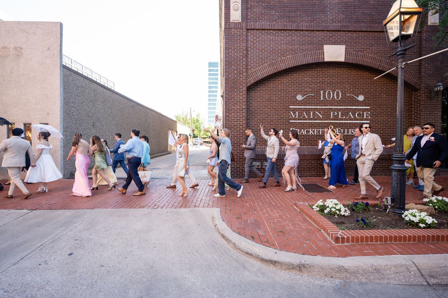 Wedding guests walking along a curved brick pathway outside a historic building at dusk.