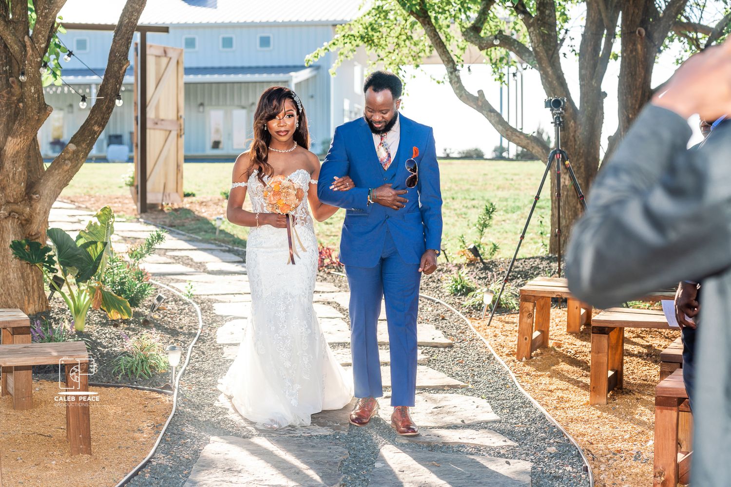 Wedding party members in blue and coral attire pose together outdoors near wooden benches.