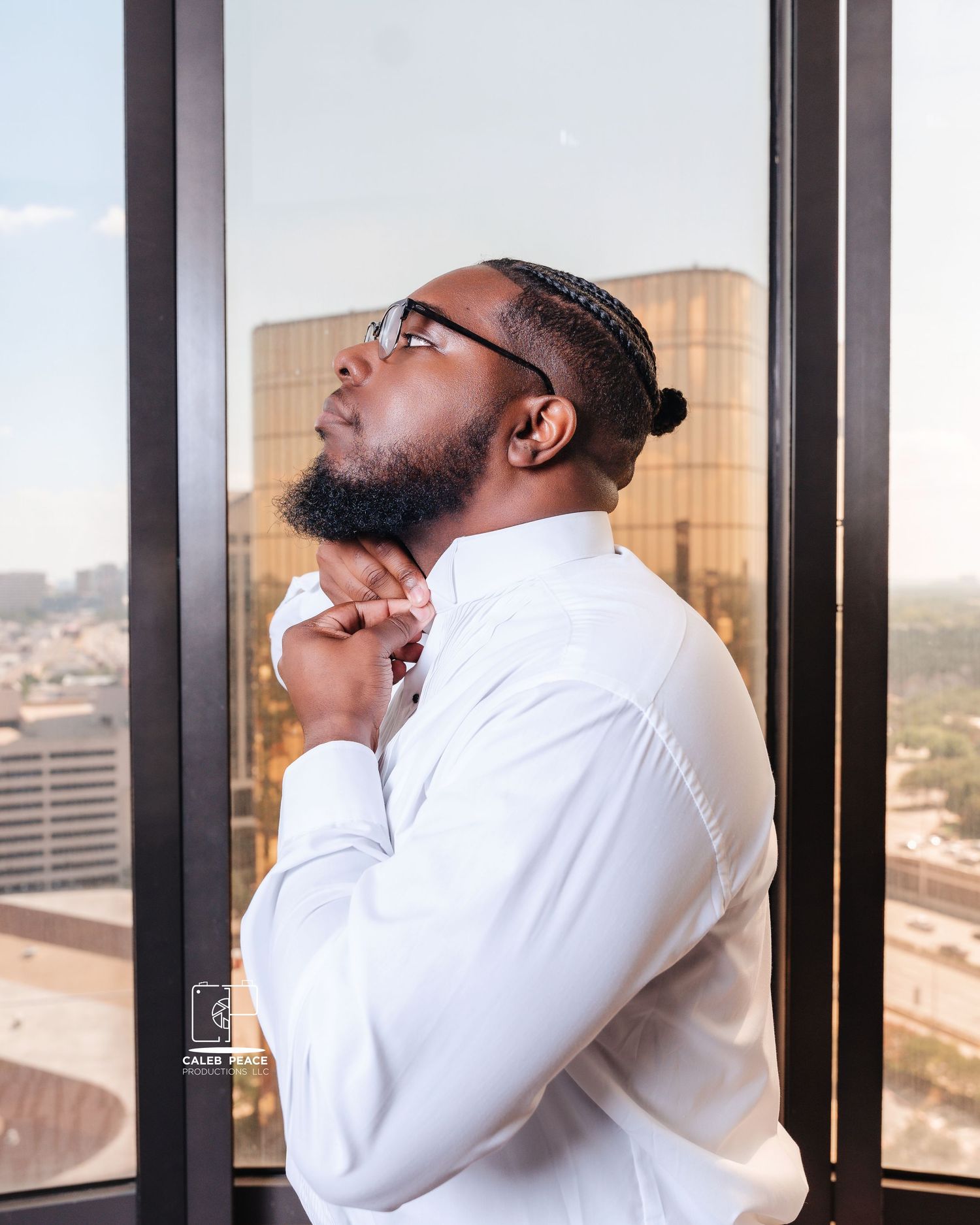 Groom adjusting tie and preparing for ceremony with city skyline visible through windows.