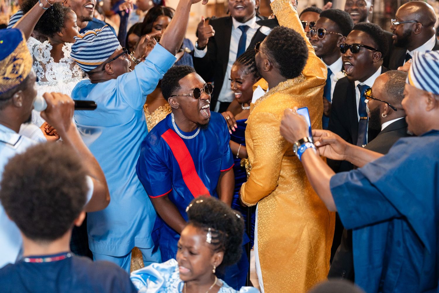 Excited wedding guests celebrating and dancing at a reception with raised hands and joyful expressions.