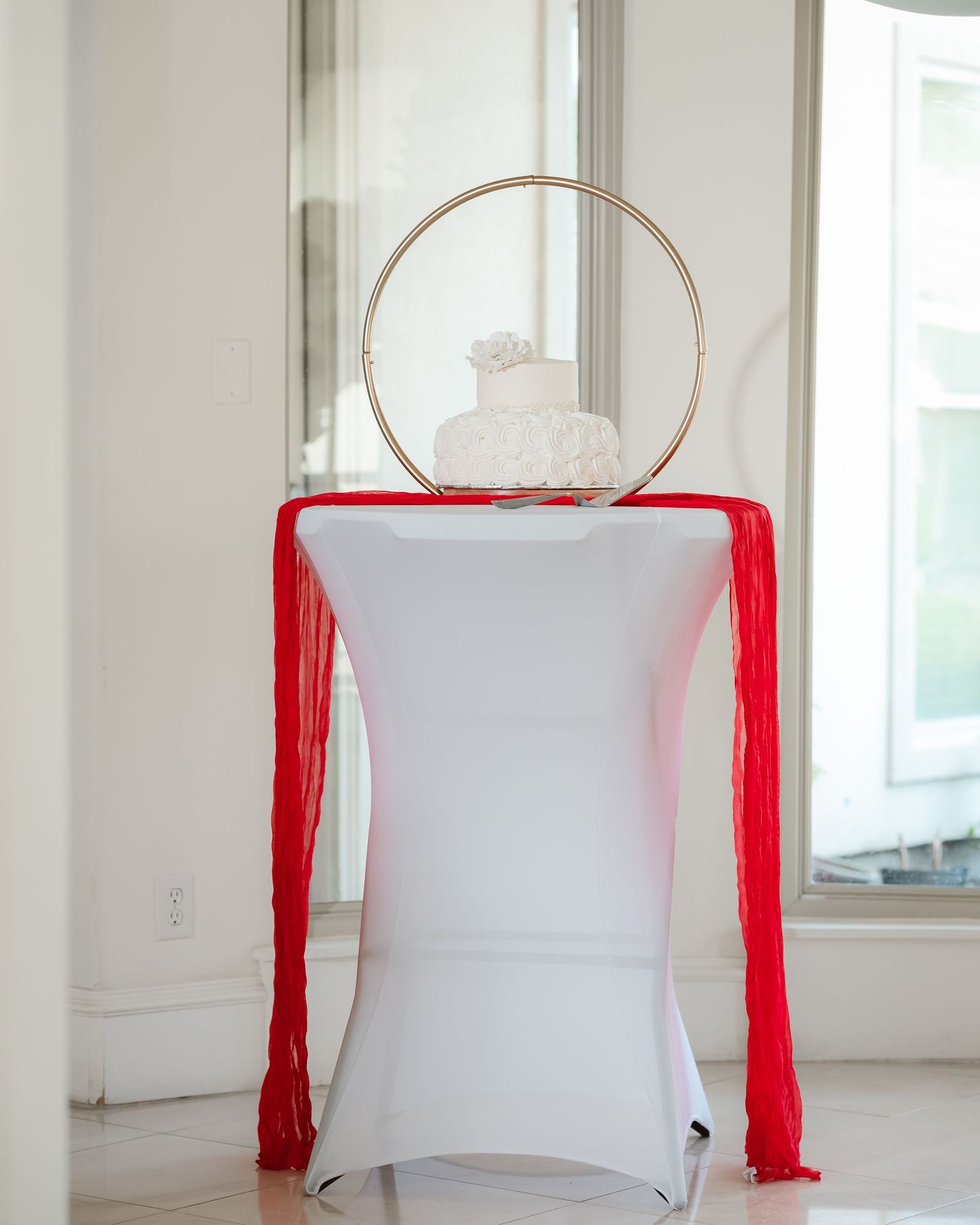Minimalist white room with red fabric draping and gold hoop accents for wedding decor.