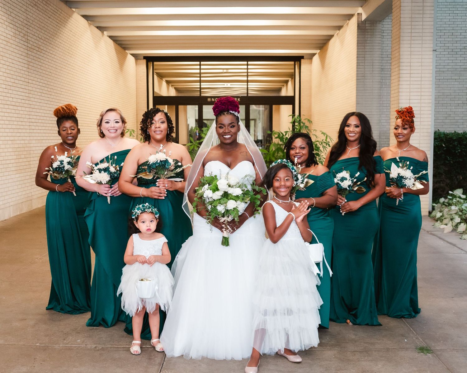 Wedding party poses in emerald green dresses and formal attire outside a modern building.