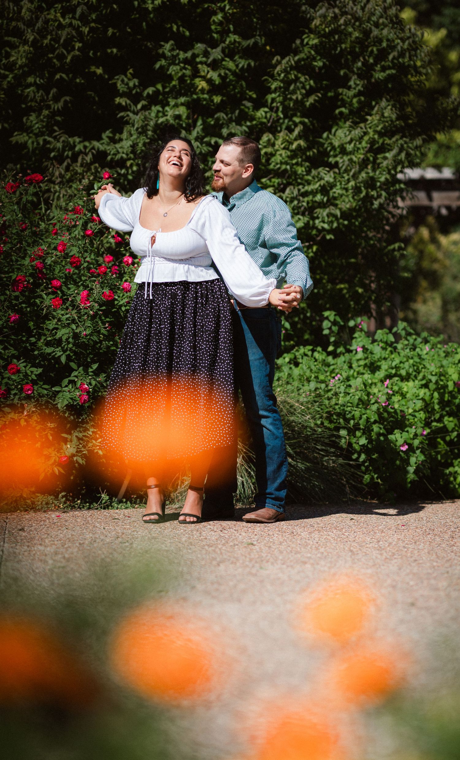 A couple shares a romantic moment together on a garden path with orange flowers in the foreground.