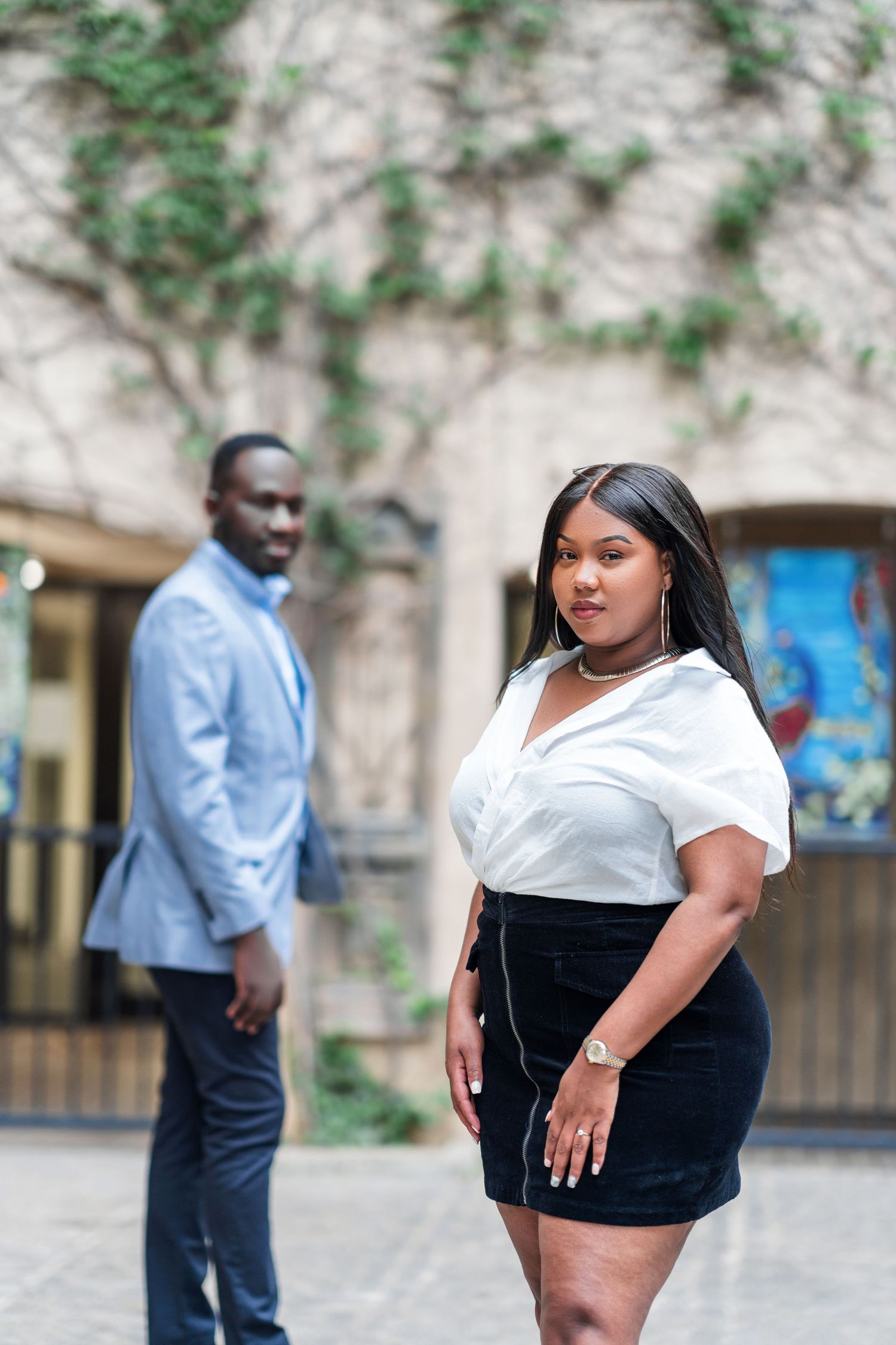 Two people in business casual attire pose outdoors against a light colored wall with climbing vines.