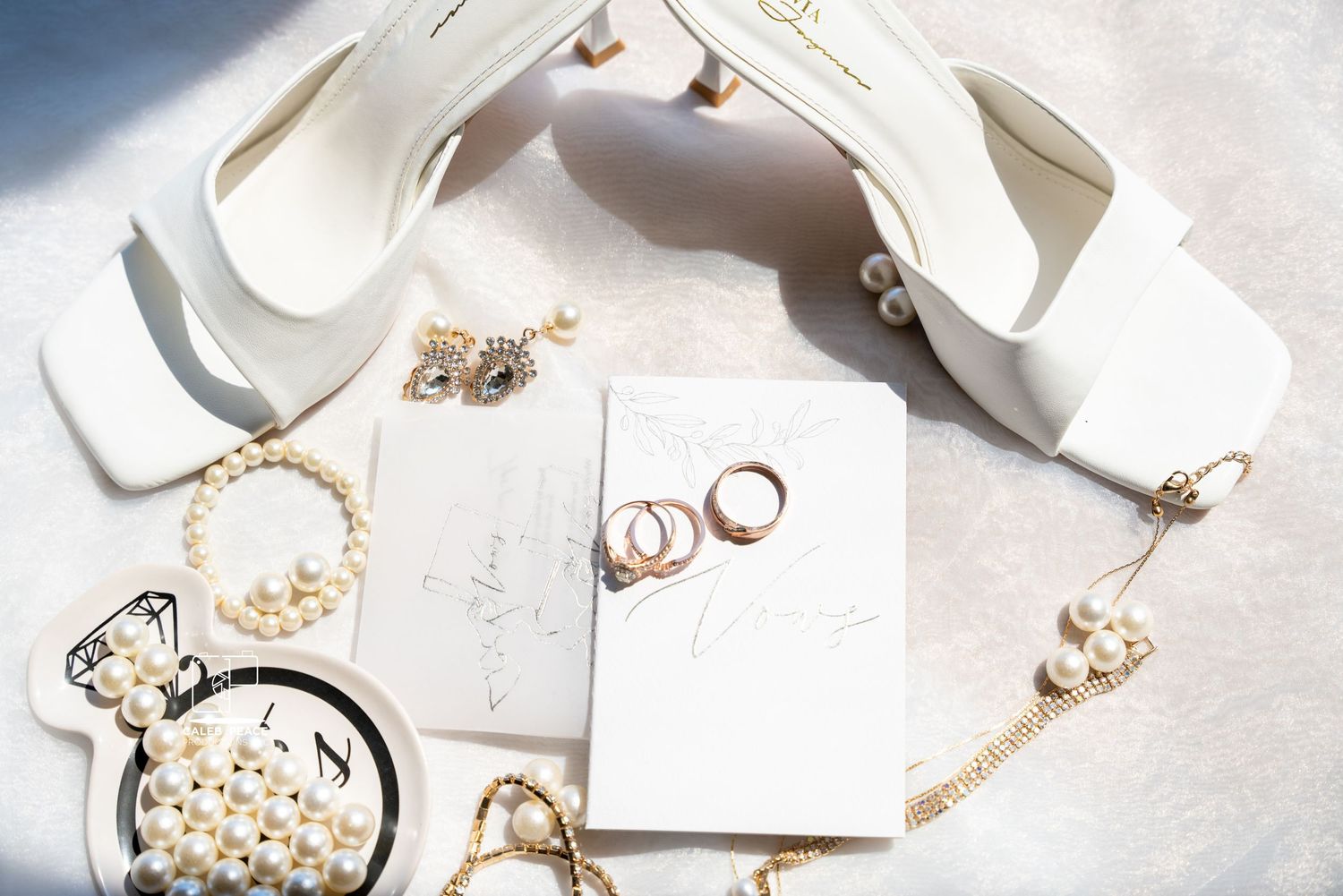 Elegant white and gold wedding accessories including shoes, jewelry, and stationery arranged on a light marble surface.