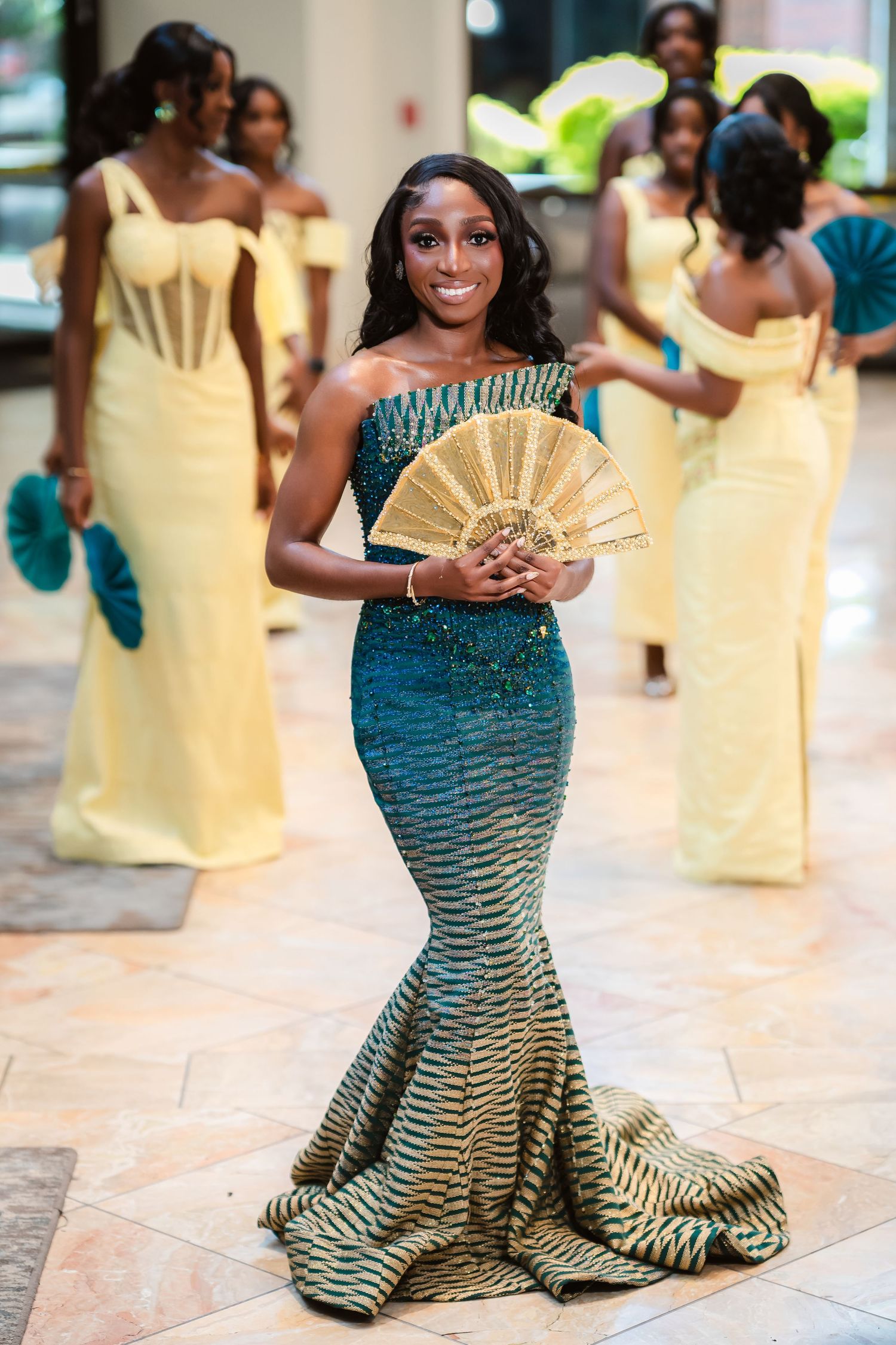 A woman in a stunning teal mermaid gown poses with a decorative fan.