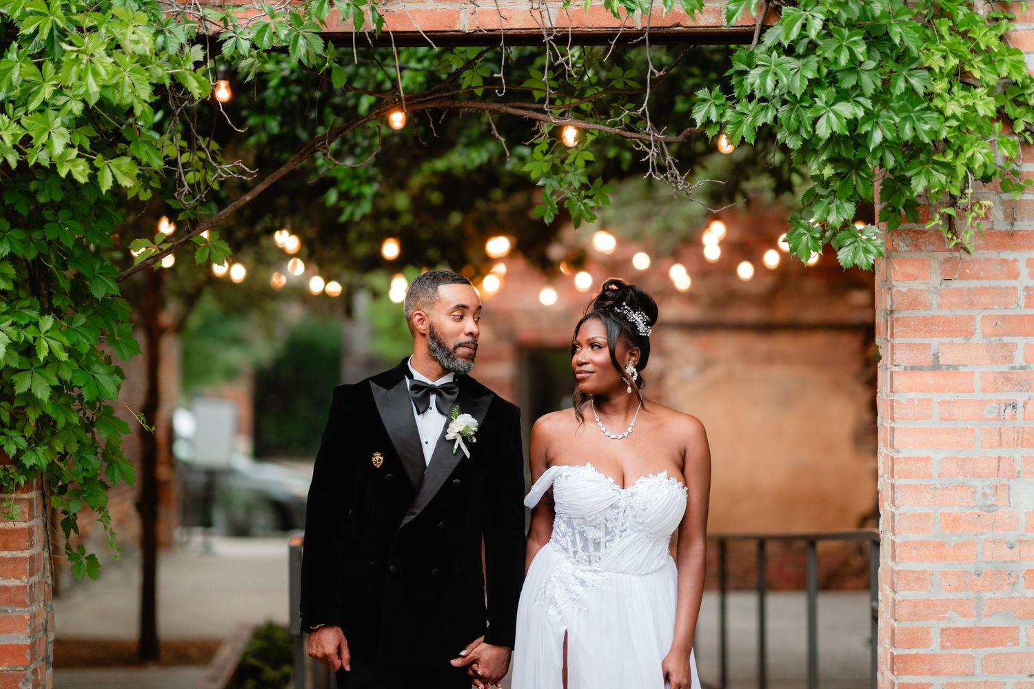 Elegant wedding portrait taken under string lights and green foliage with a romantic garden setting.