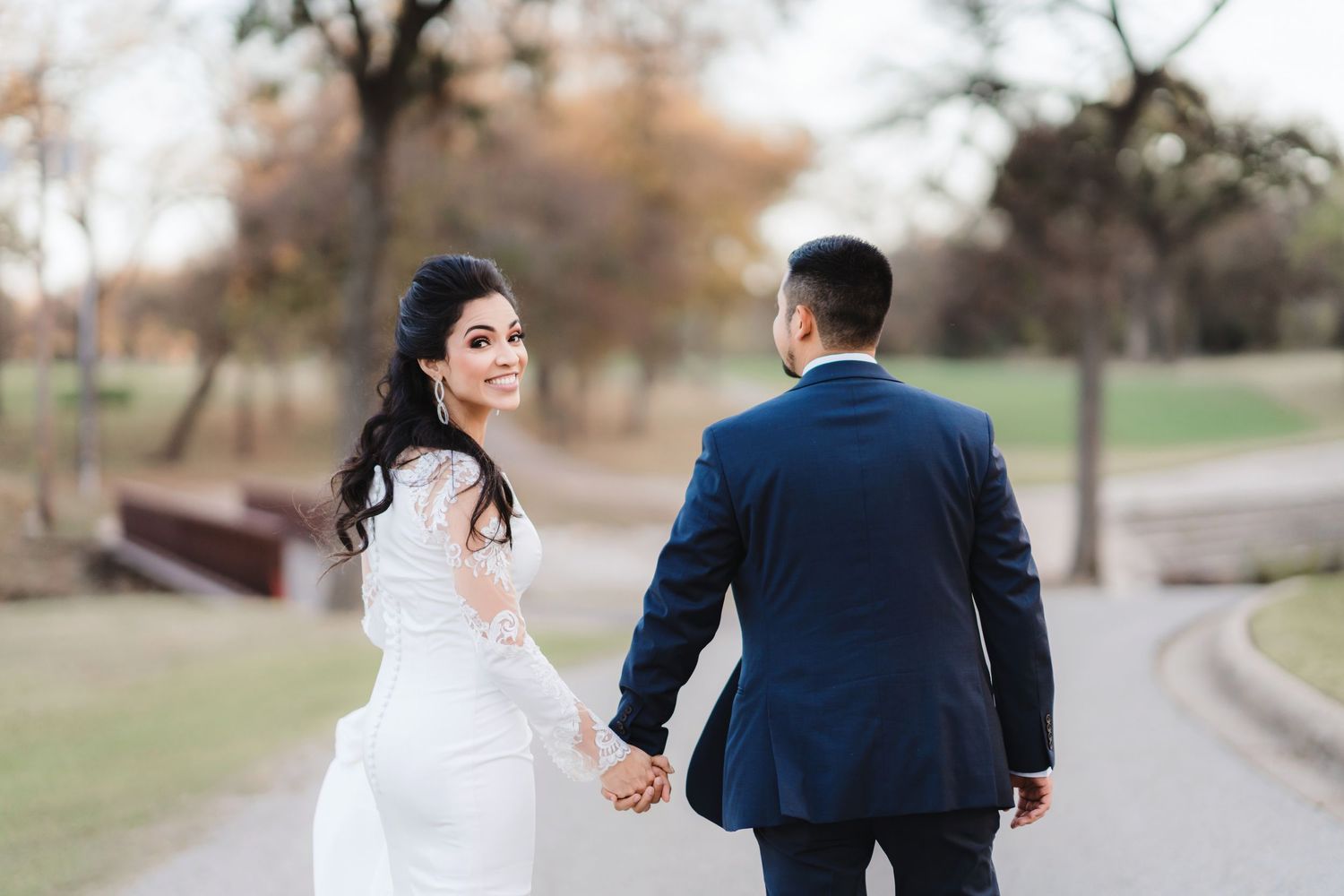 Wedding couple walking together outdoors with bride in white dress and groom in navy suit.