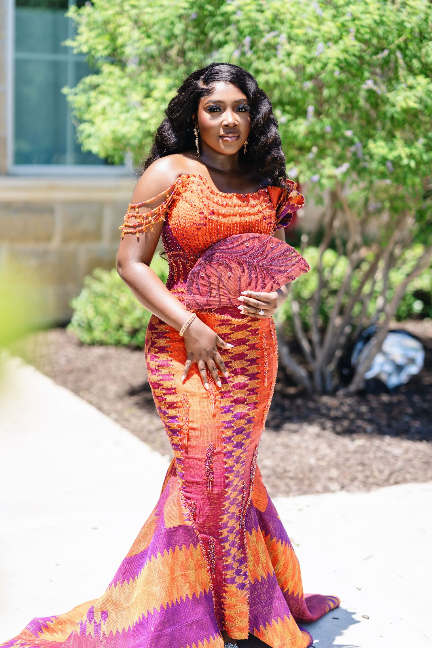 Traditional African wedding attire featuring vibrant orange and purple kente cloth patterns photographed outdoors.