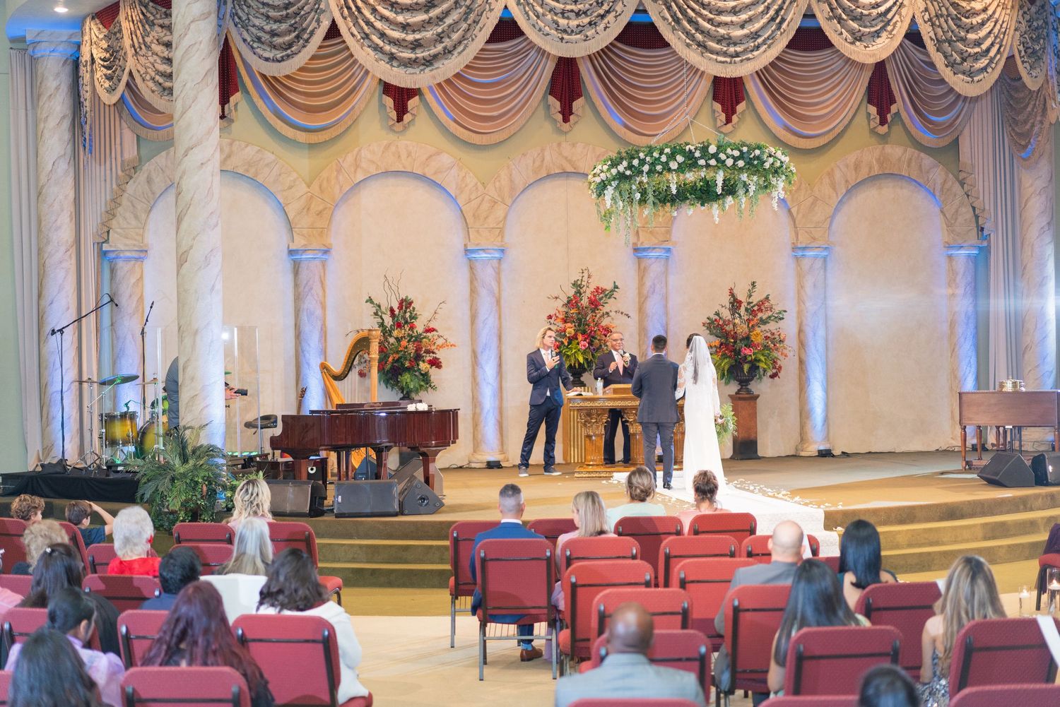 Elegant wedding venue with ornate draping, red chairs, and grand architectural details.