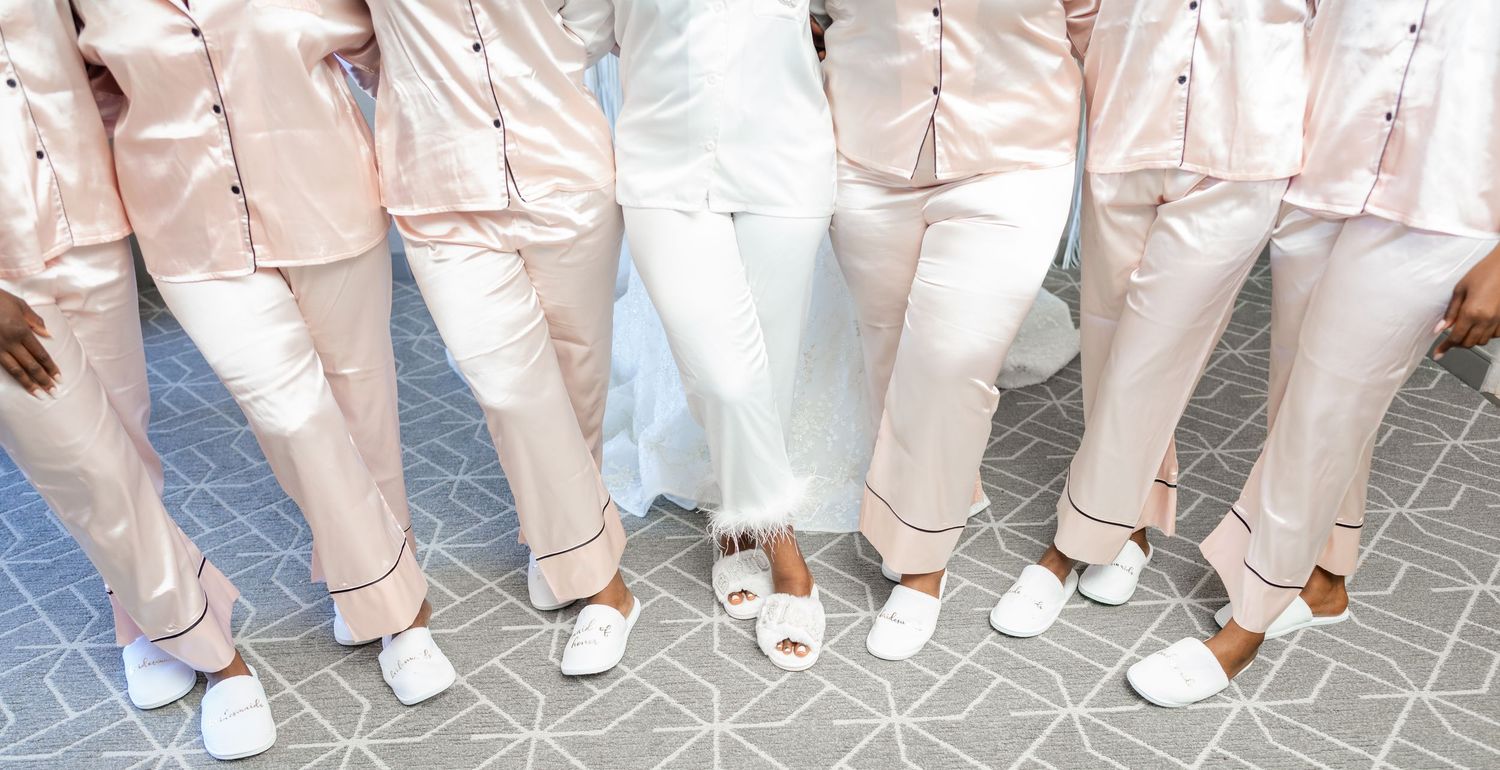 A row of groomsmen in light pink suits and white sneakers stand in matching poses on a gray floor.