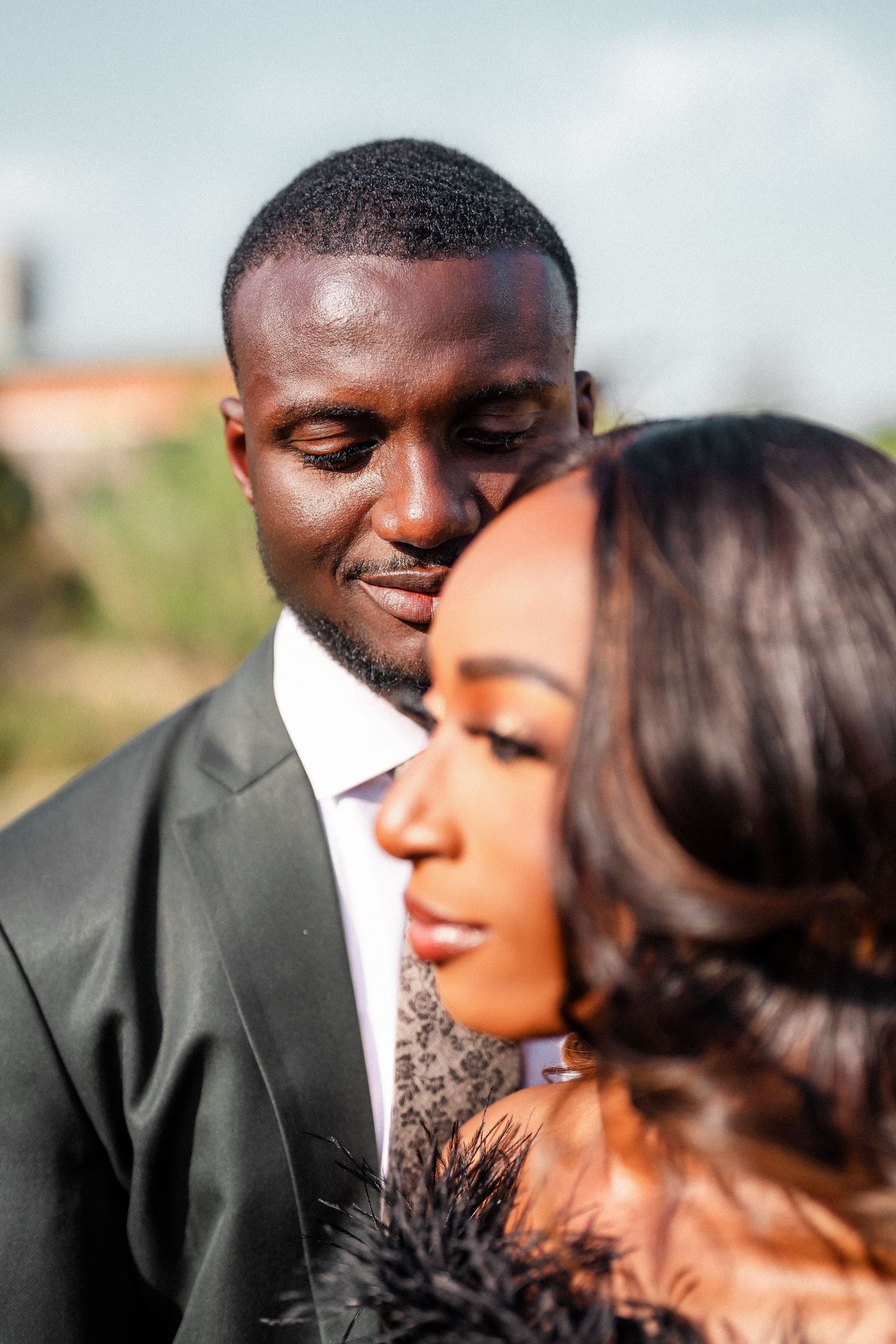 A romantic couple in formal attire share an intimate moment outdoors during a photoshoot.