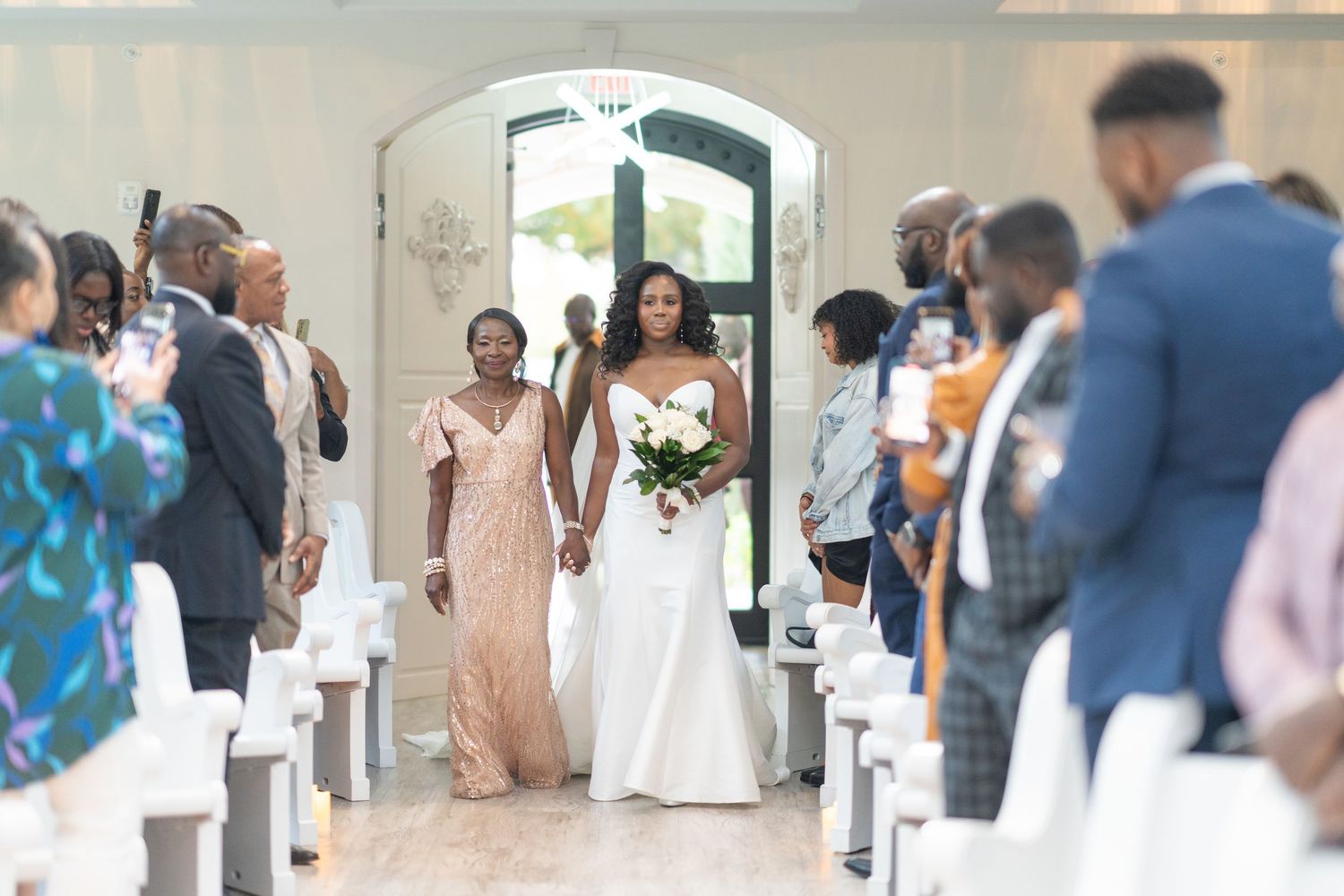 Wedding guests seated in white chairs during an indoor ceremony celebration.