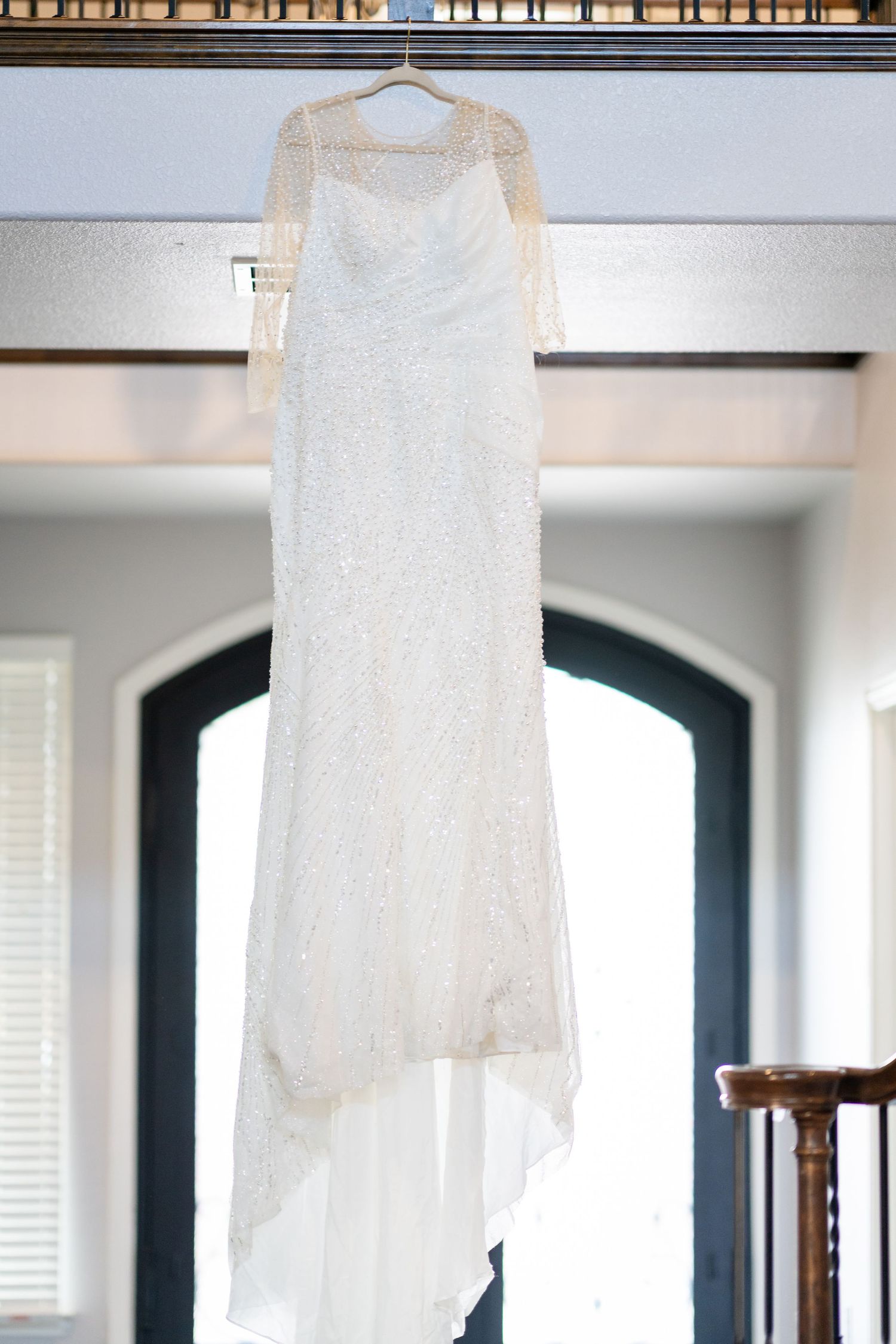 An elegant white lace wedding dress hangs on display in a doorway.